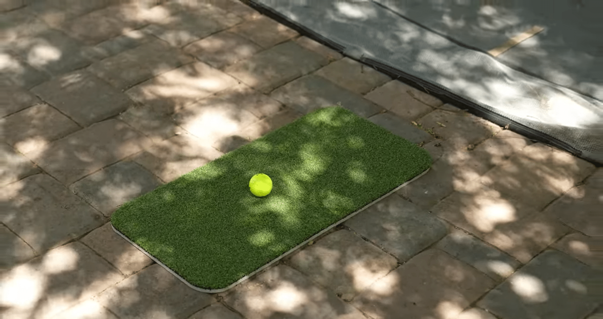Tennis ball on small green mat outdoors