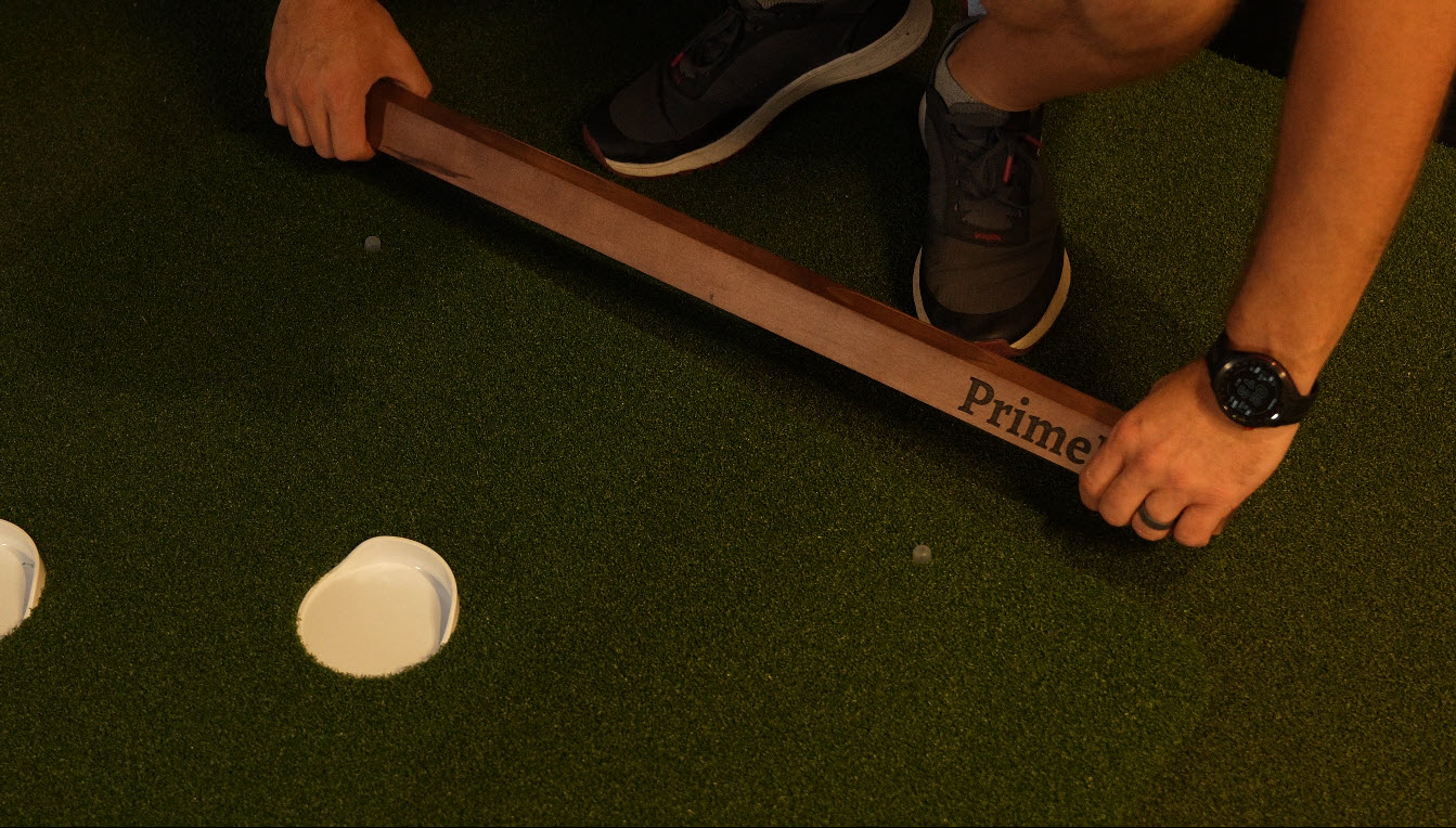 Person positioning wooden putting guide on artificial turf