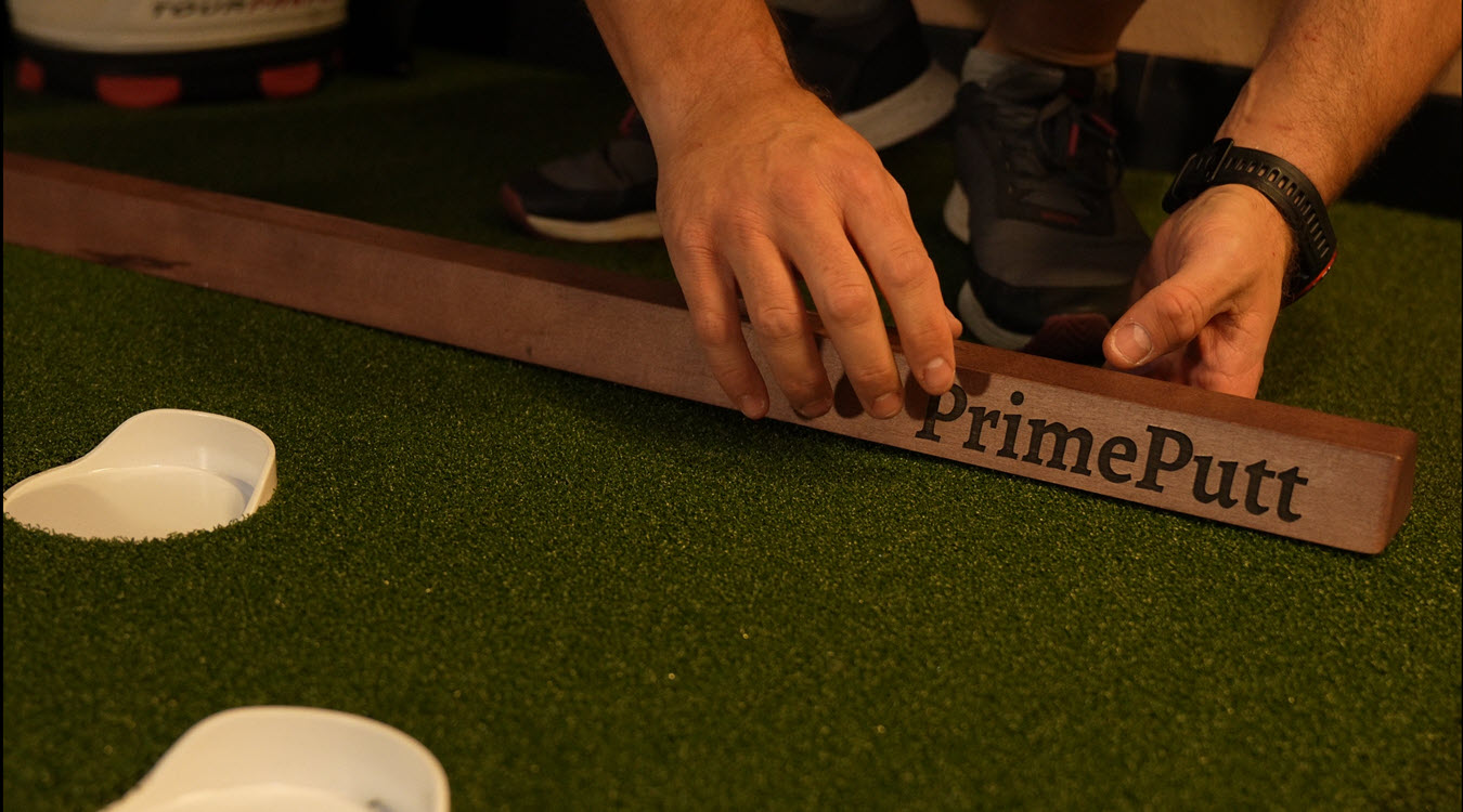 Hands positioning PrimePutt training rail beside golf hole