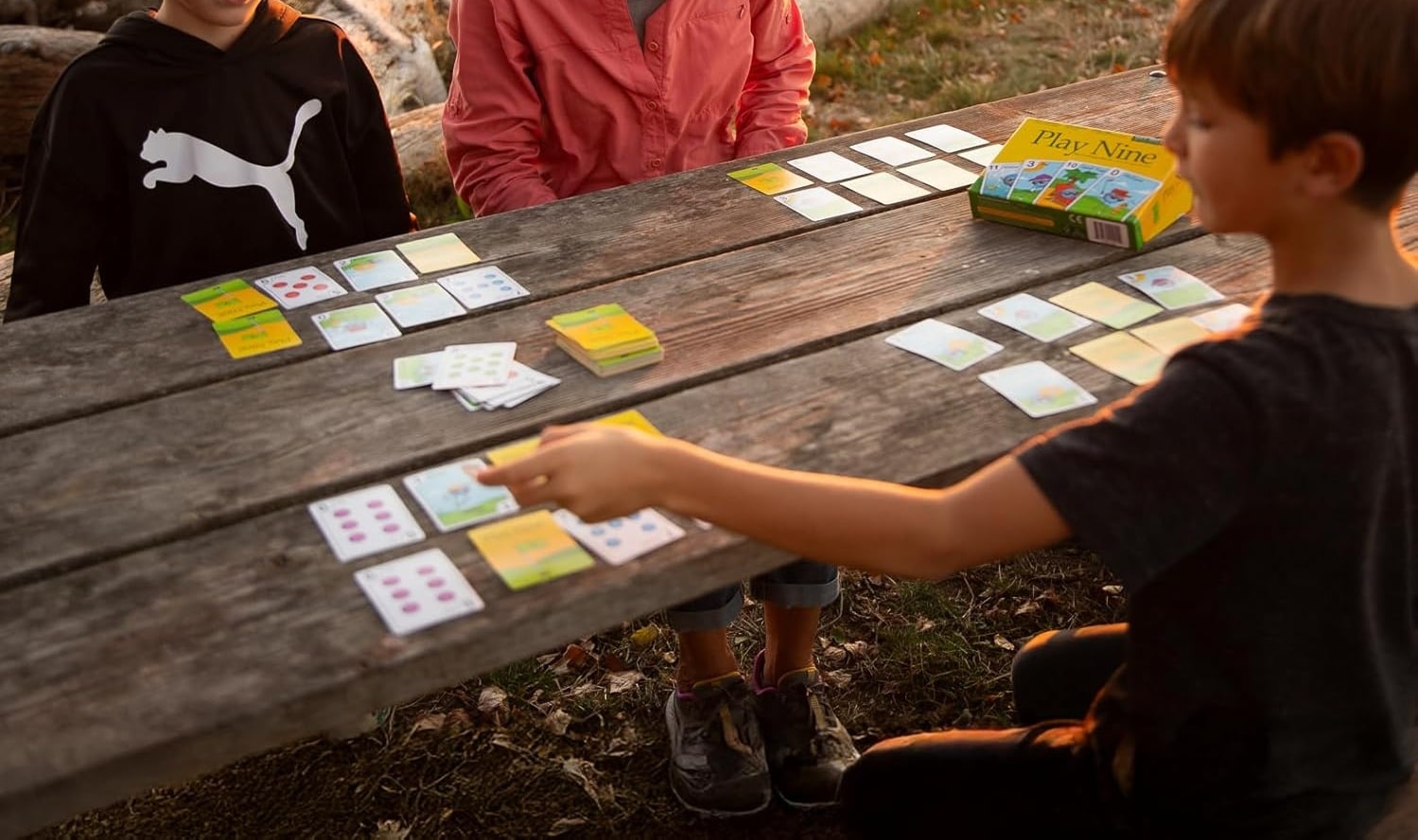 Children playing a card game outdoors at sunset.