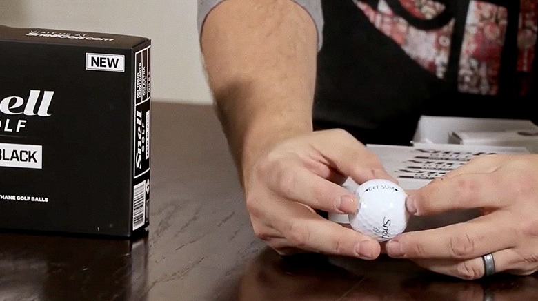 Person holding a golf ball beside a box.