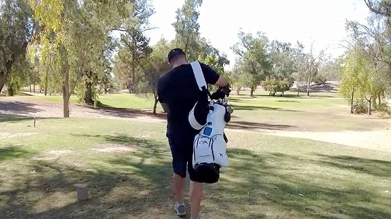 Person walking on golf course carrying golf bag.