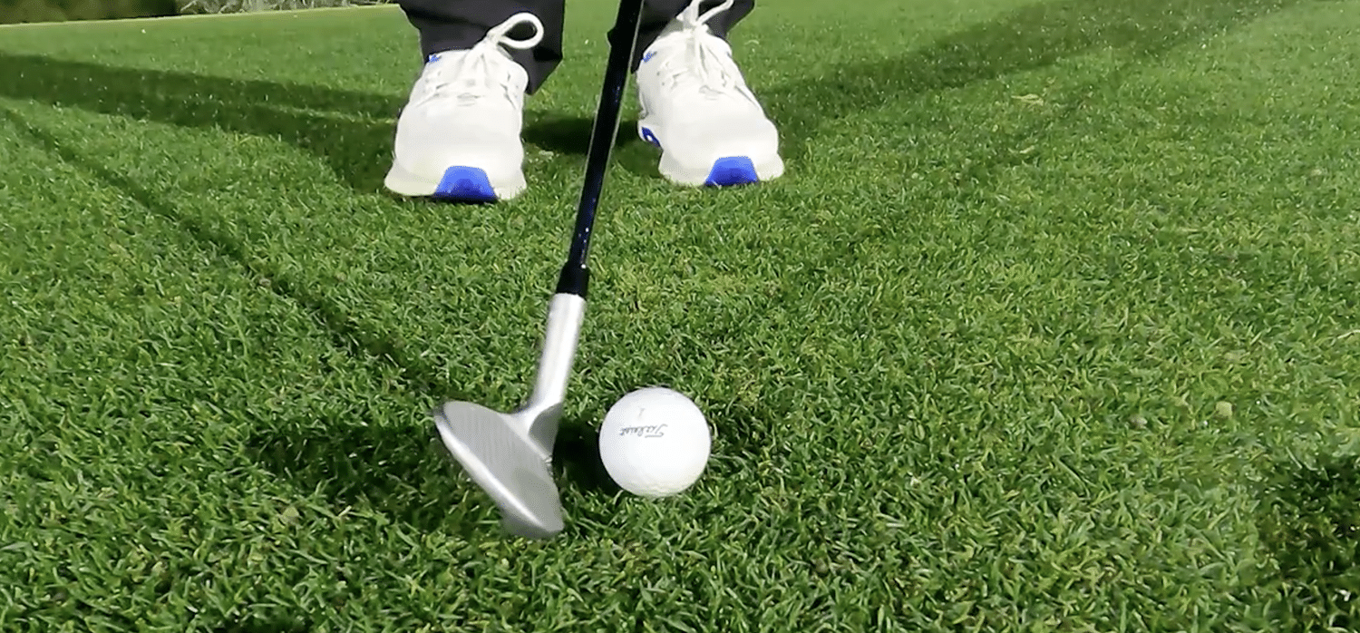 Golf club positioned over a golf ball on grass
