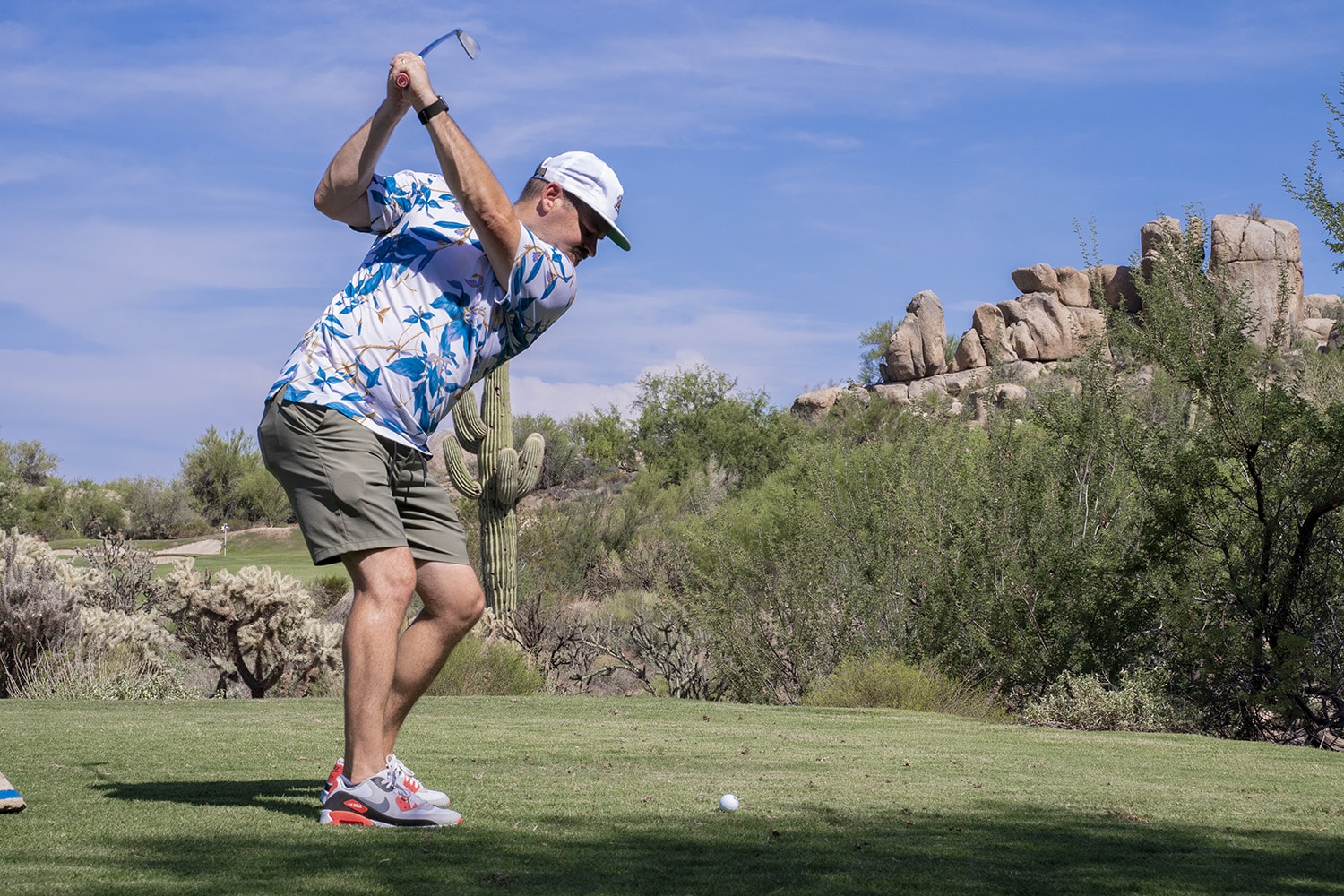 Golfer swinging in a desert landscape.