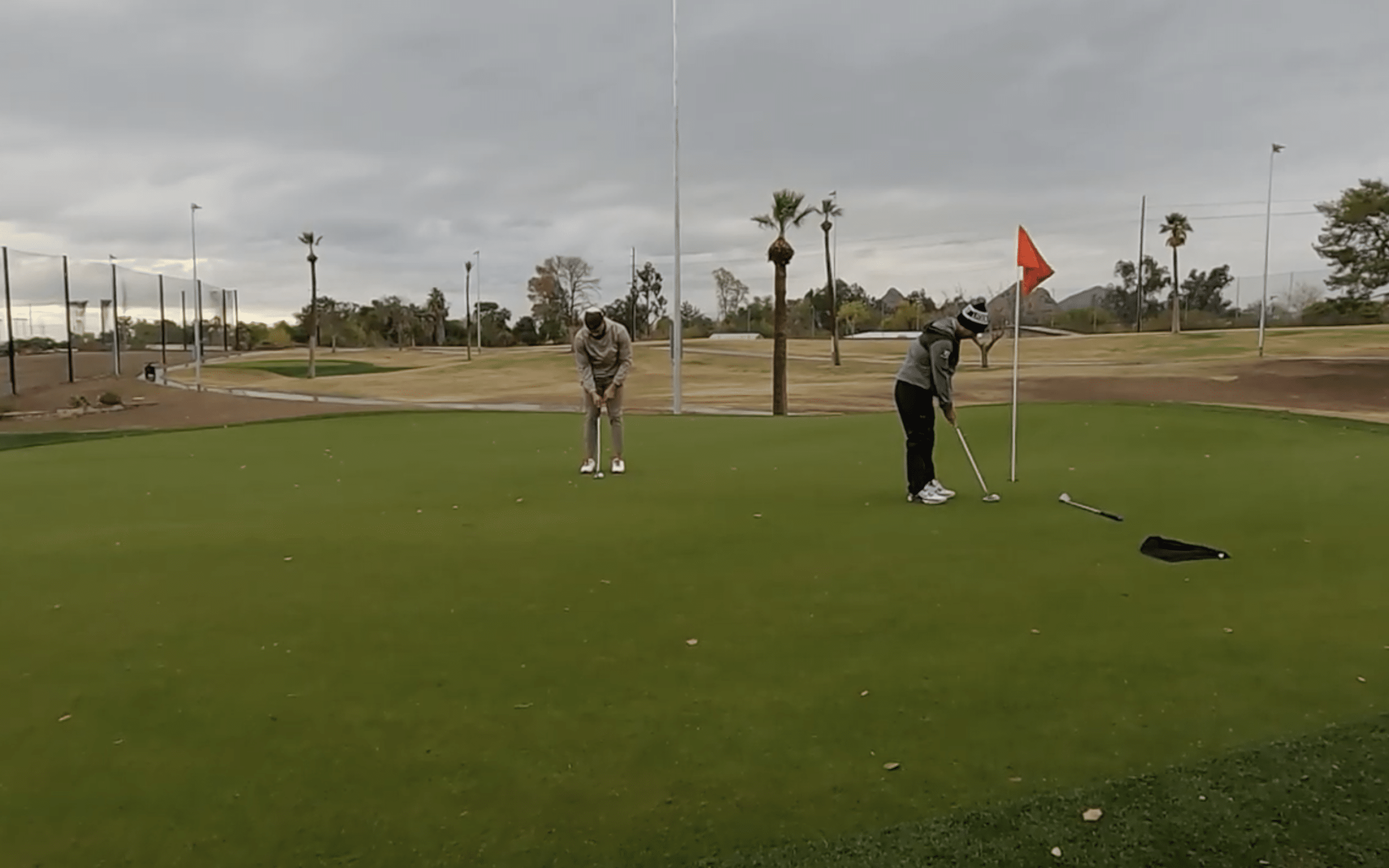 Two golfers putting on a green under cloudy sky.