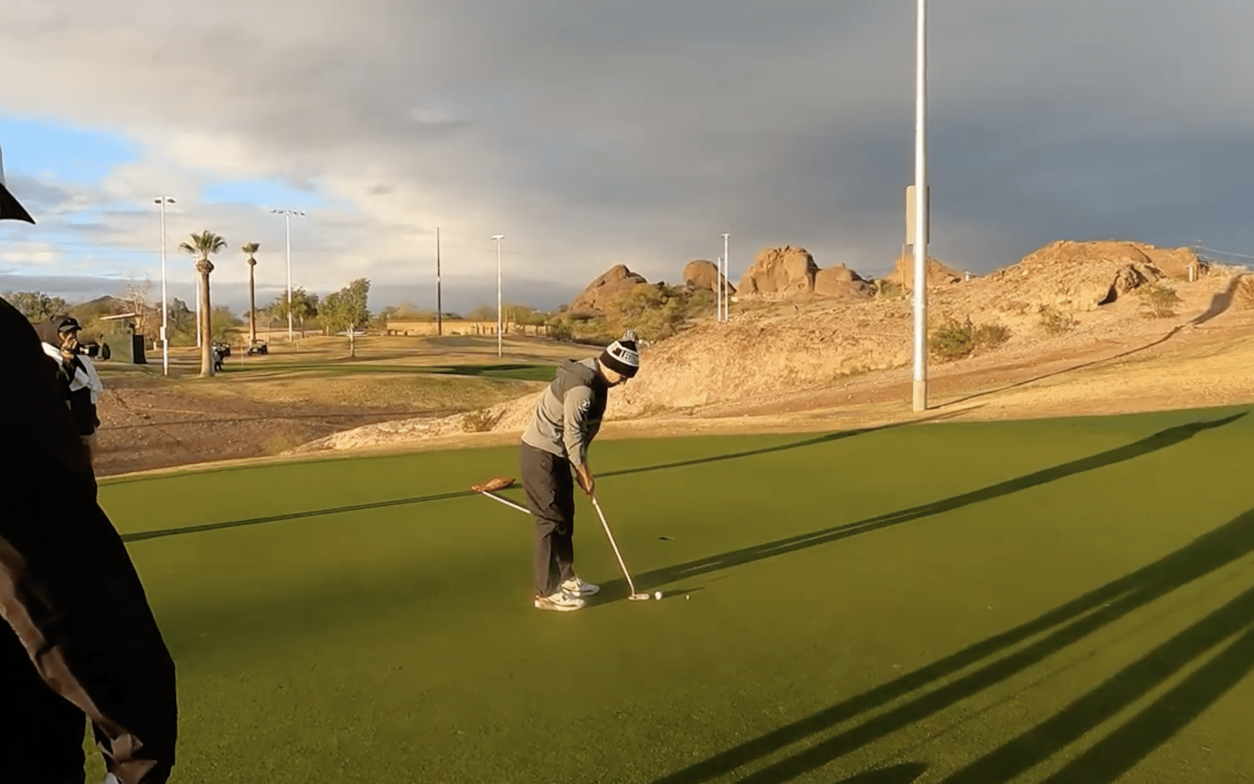 Golfer putting on a green landscape with rocks.