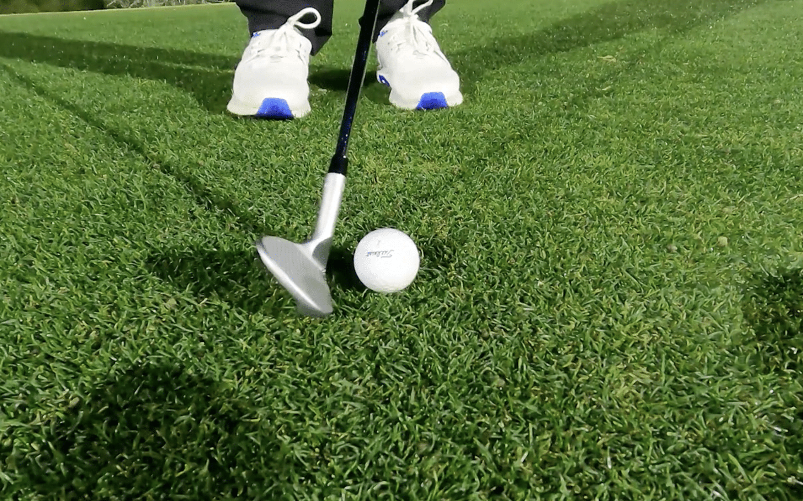 Golf club poised above a golf ball on grass.