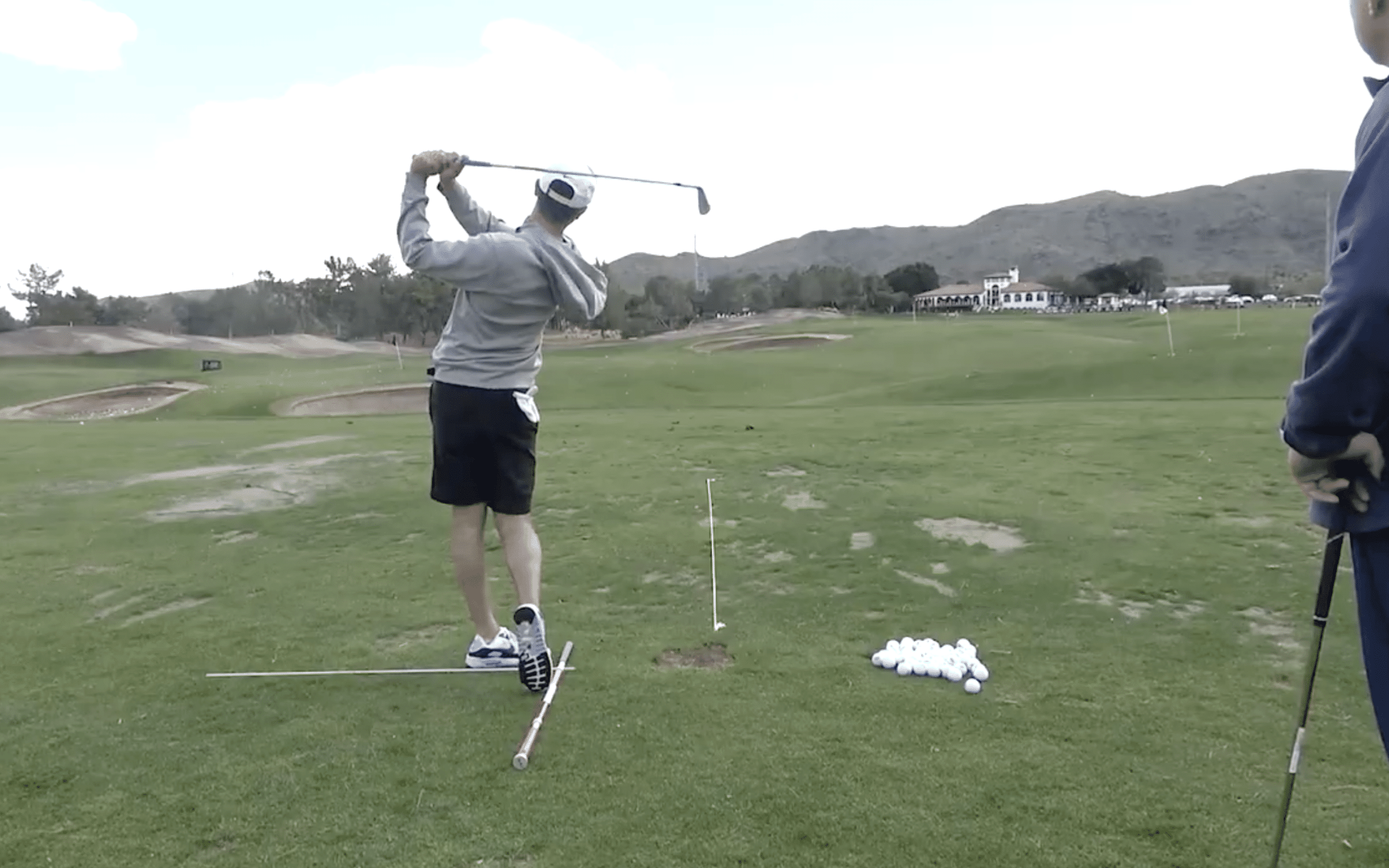 Golfer practicing swing on driving range.