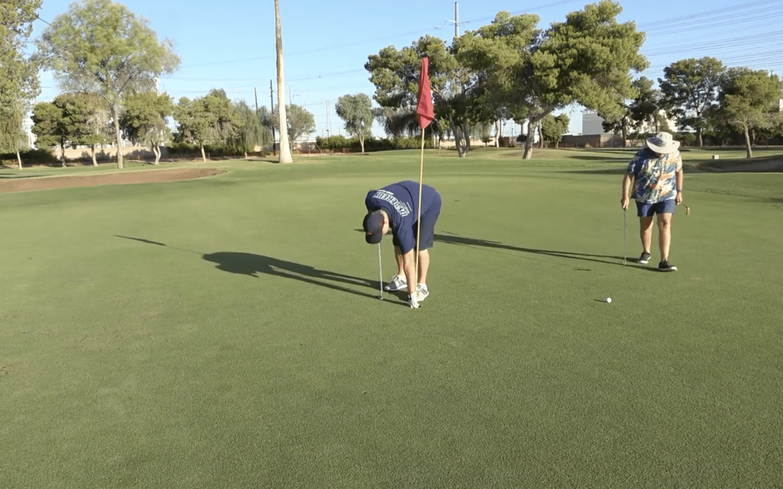 Two golfers on a green preparing to putt.