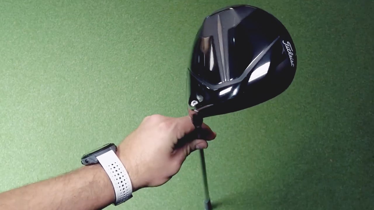 Person holding a golf driver on green surface.