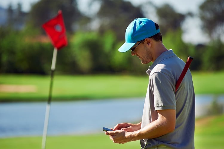 Golfer checking phone near flag on course