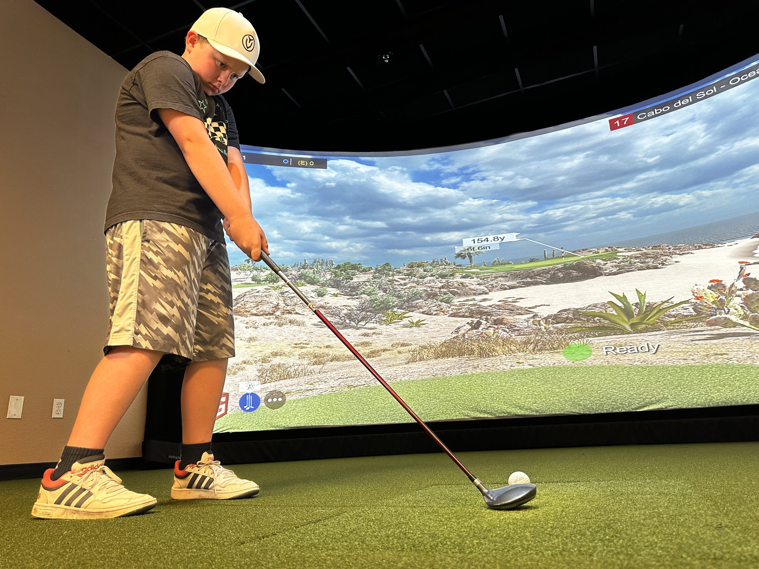 Child playing virtual golf on indoor simulator
