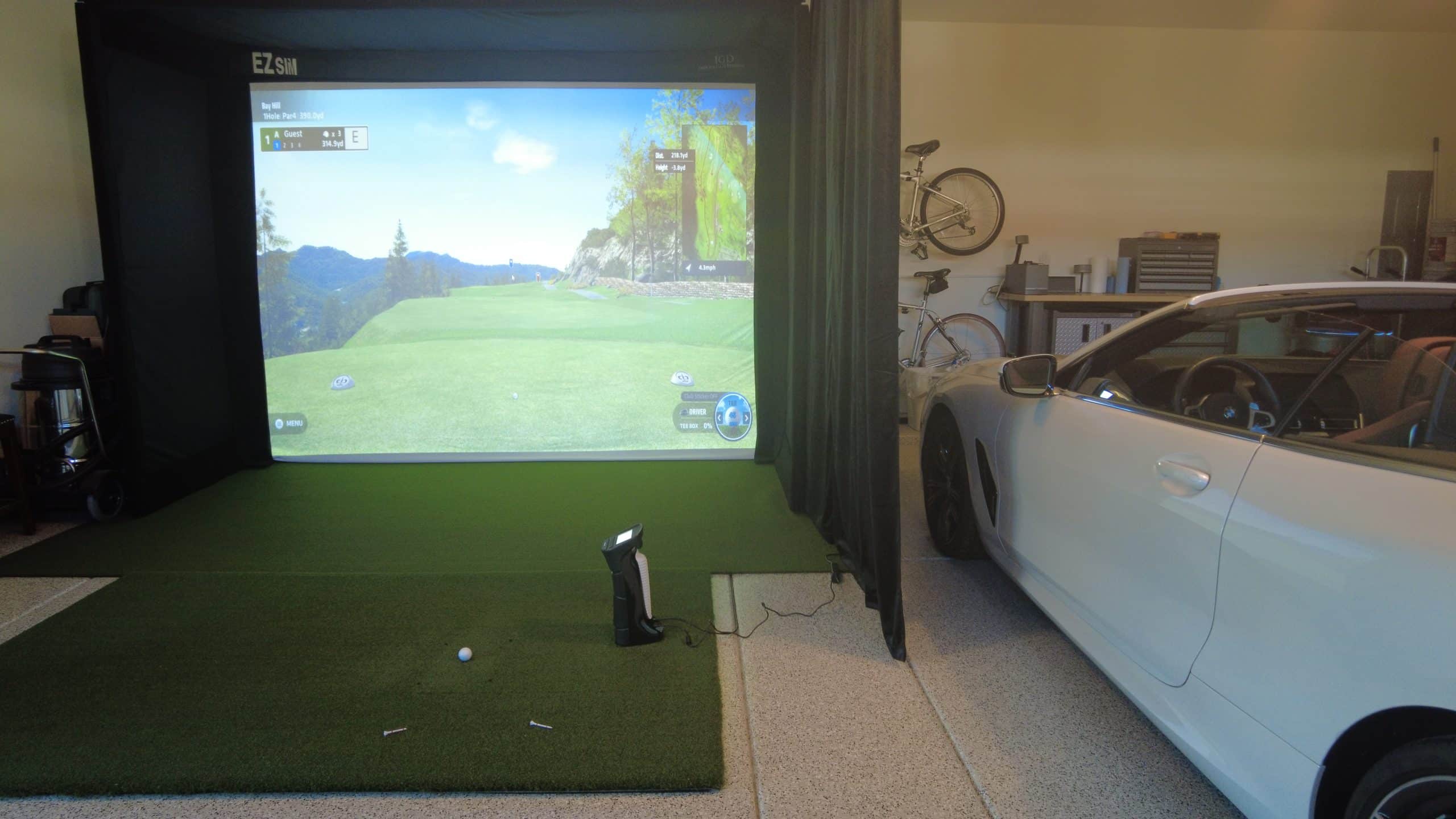Home golf simulator setup in garage with car.
