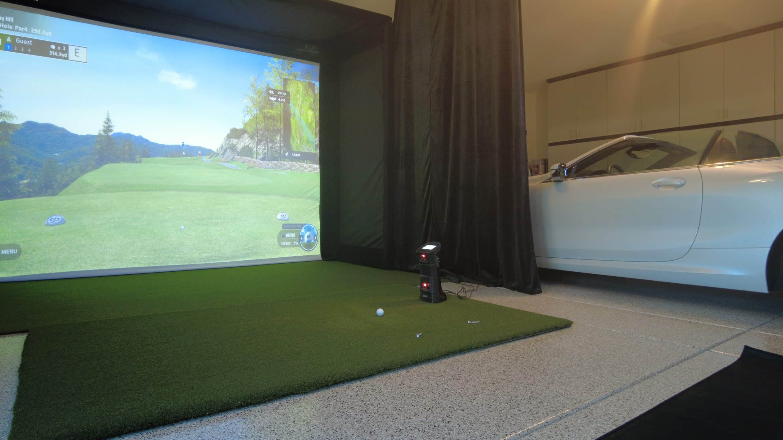 Home golf simulator setup beside white convertible car