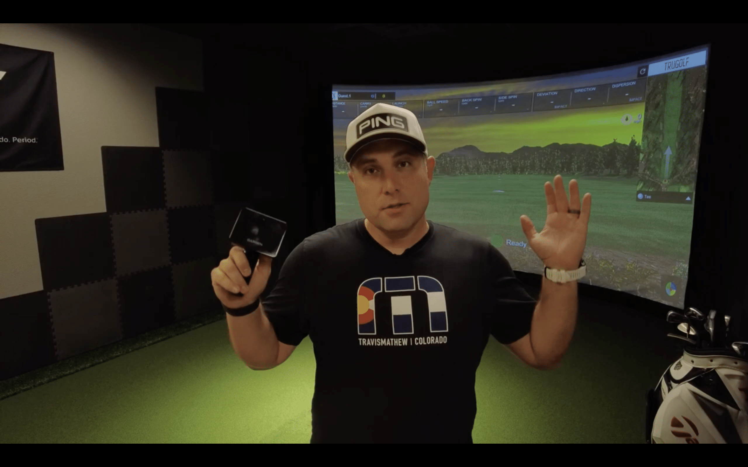 Man presenting golf simulator indoors with projector screen.