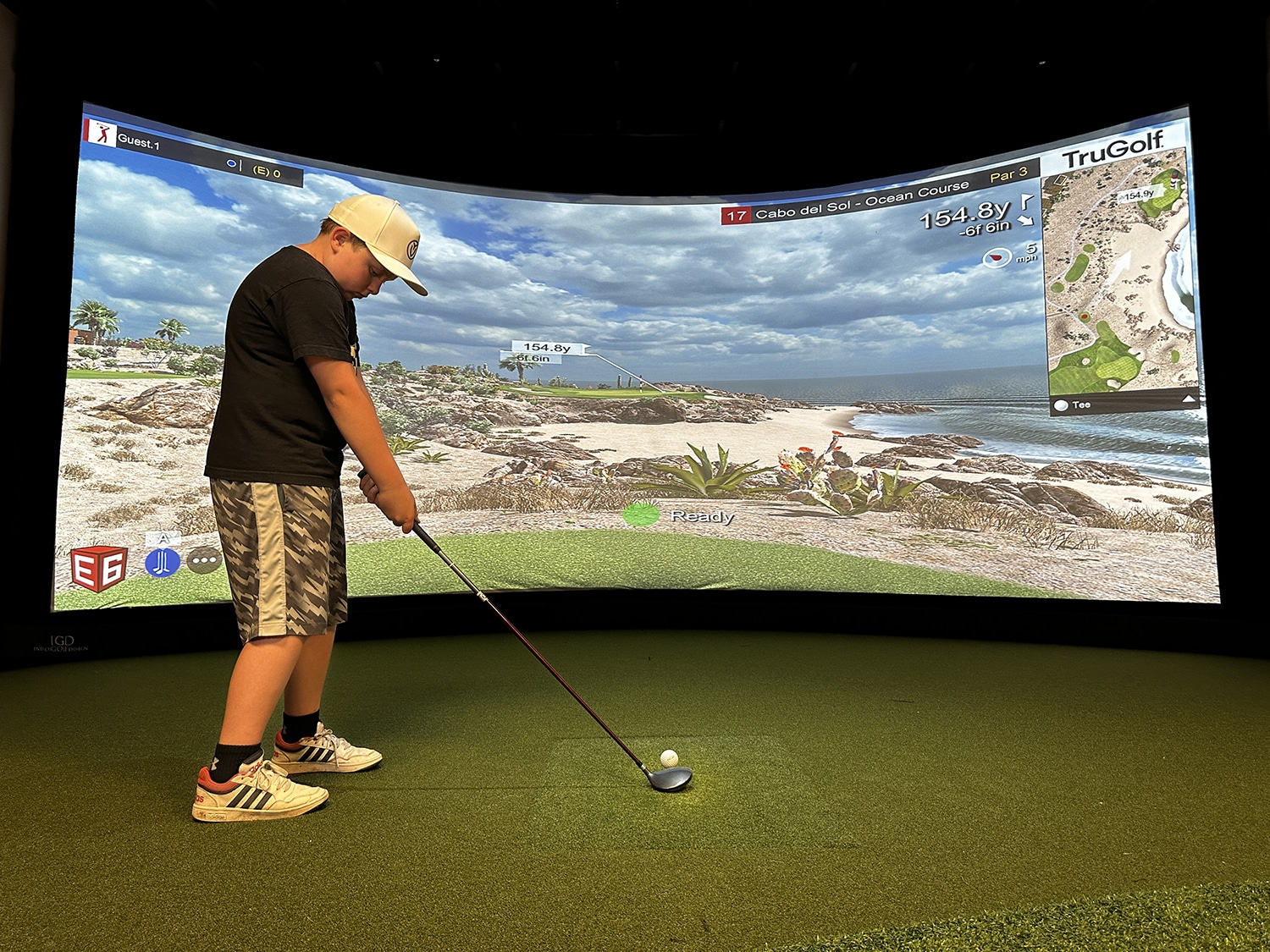 Boy playing golf on indoor simulator screen