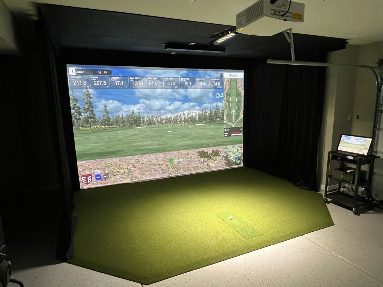 Indoor golf simulator with screen and projector setup.