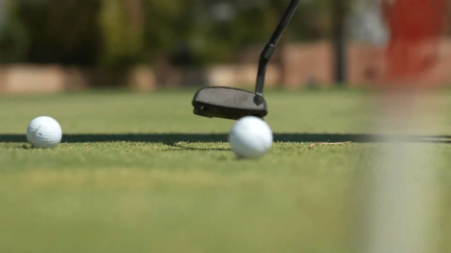 Golf putter striking ball on green course