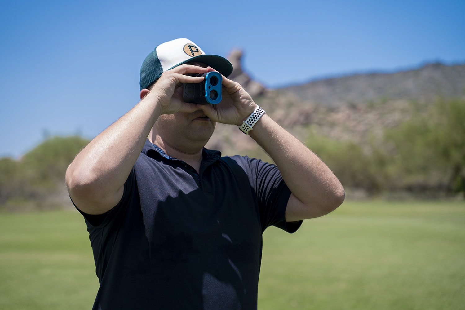 Golfer using rangefinder on sunny golf course