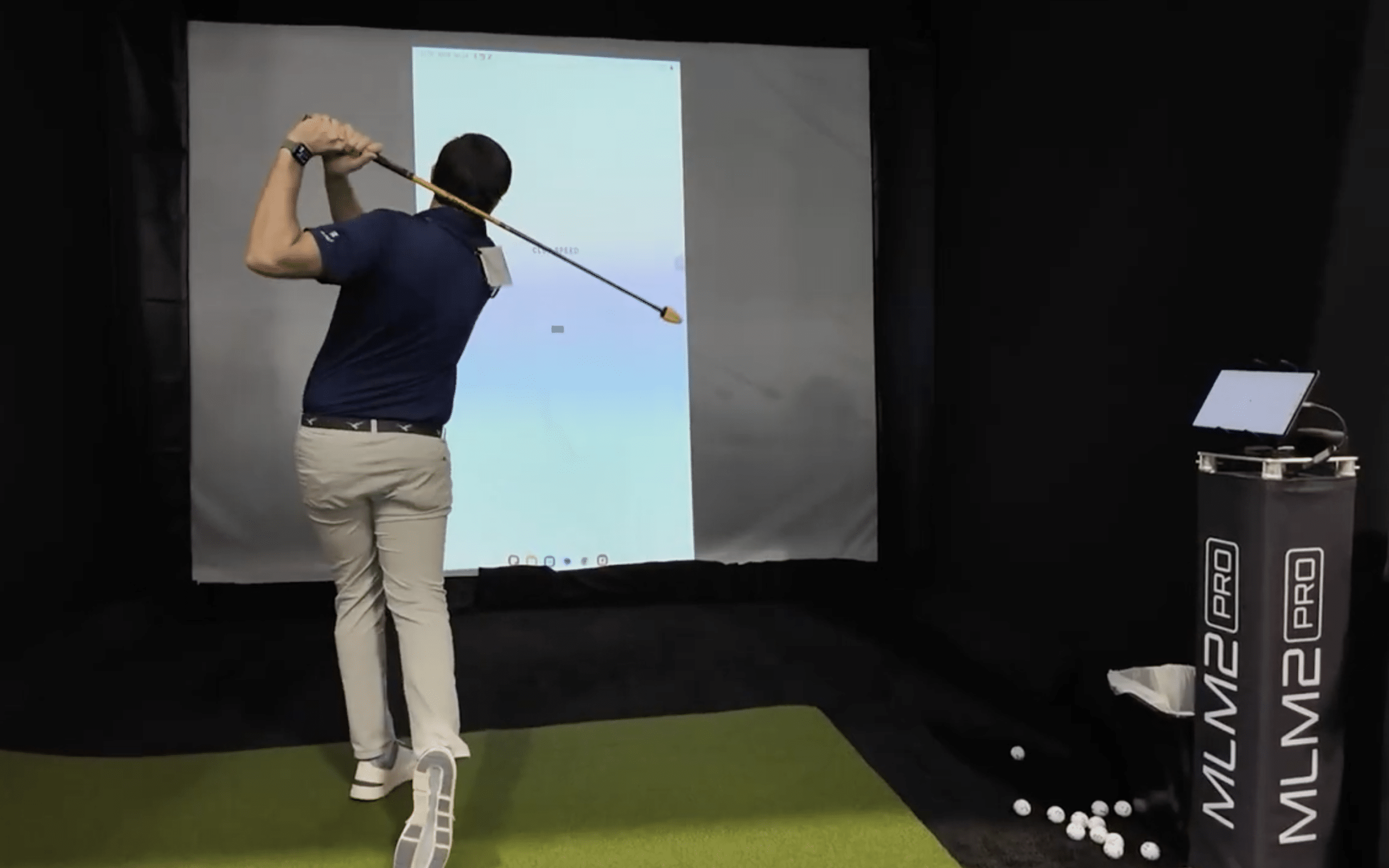 Golfer practicing swing in indoor golf simulator setup.