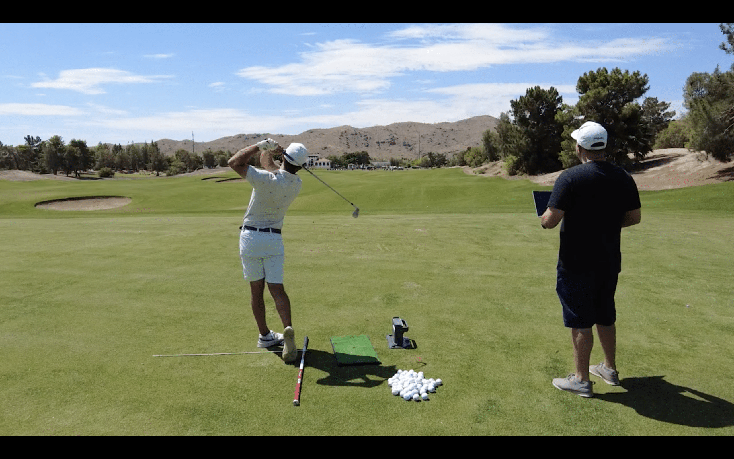 Golfer practicing swing with coach on driving range.