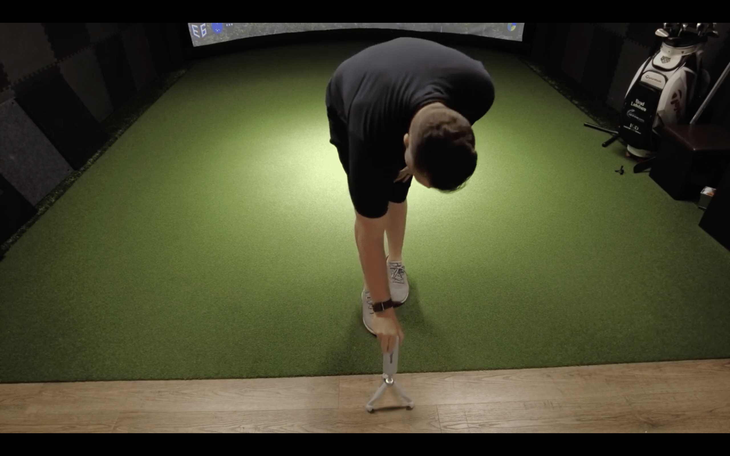 Man setting up tripod on indoor golf simulator turf