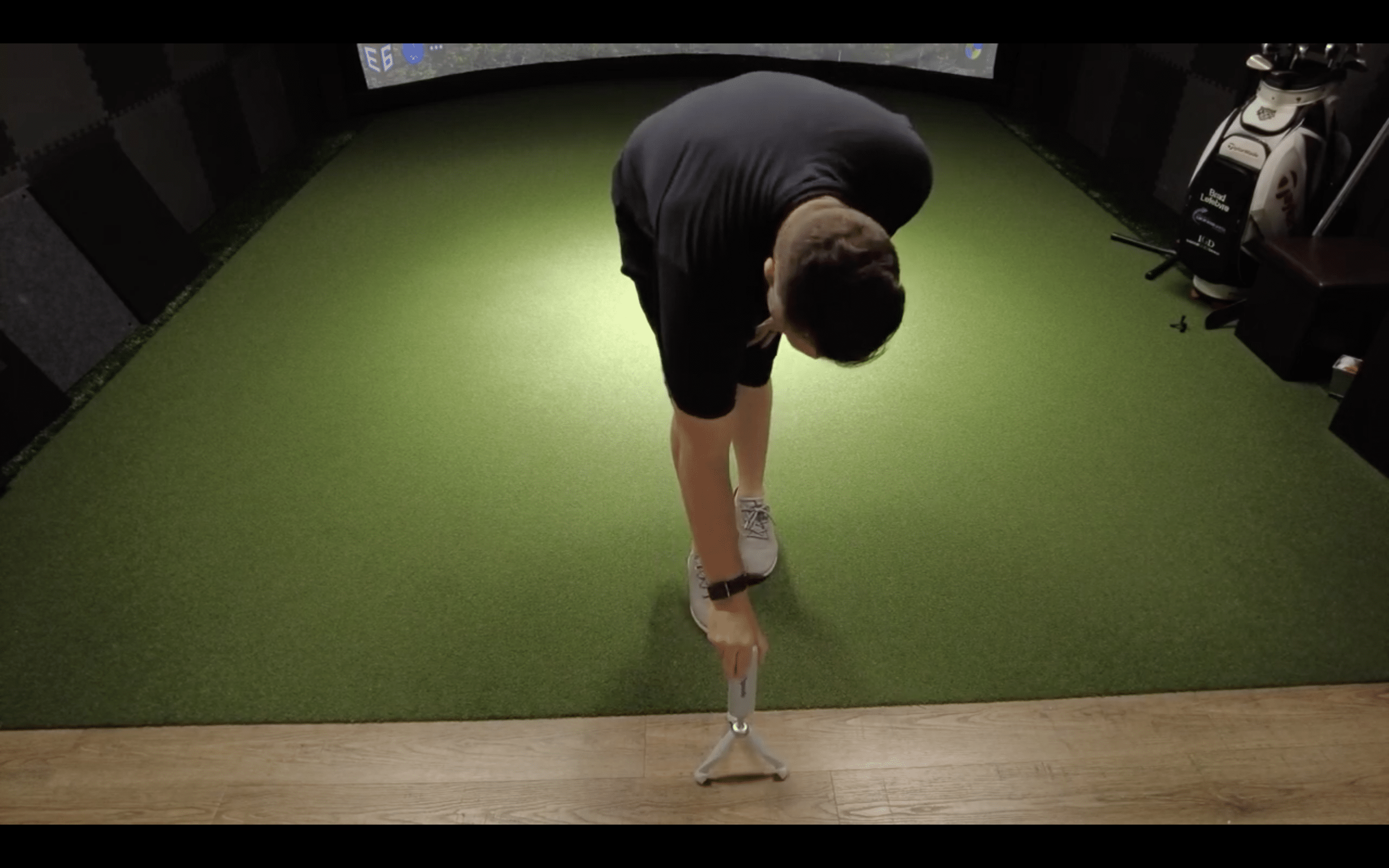 Man setting up tripod on indoor golf simulator mat
