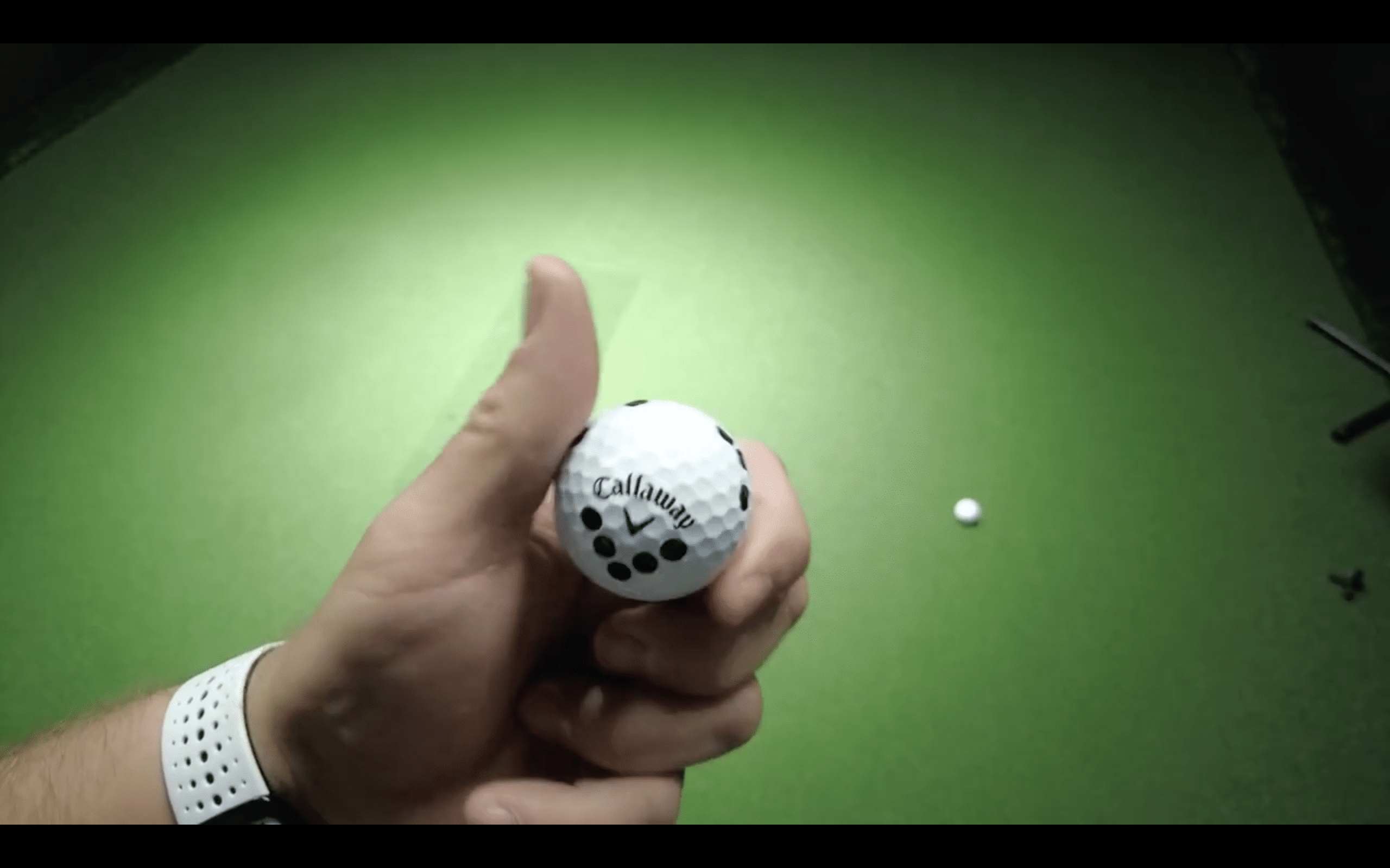 Hand holding Callaway golf ball on green surface