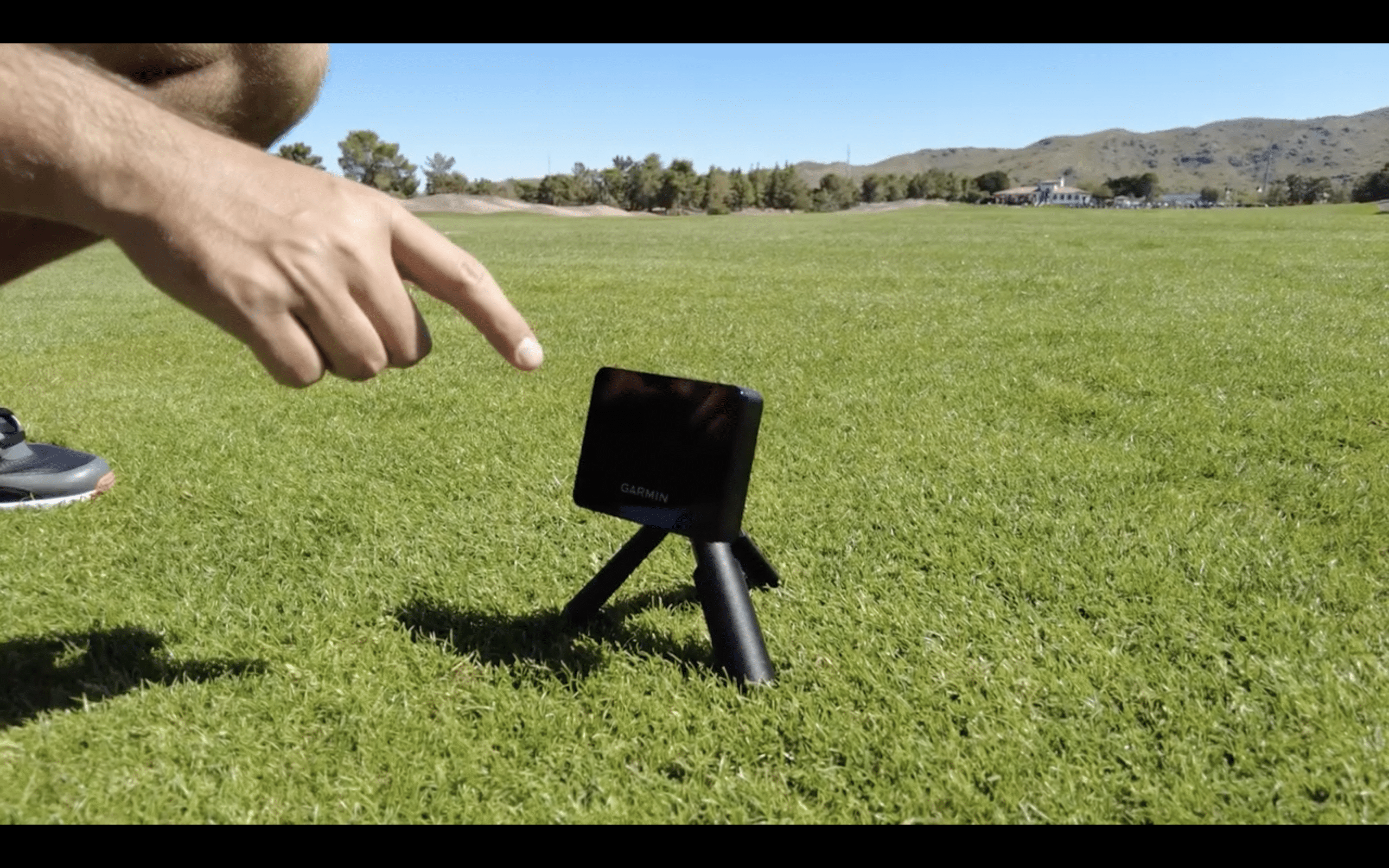 Person pointing at Garmin device on grass field