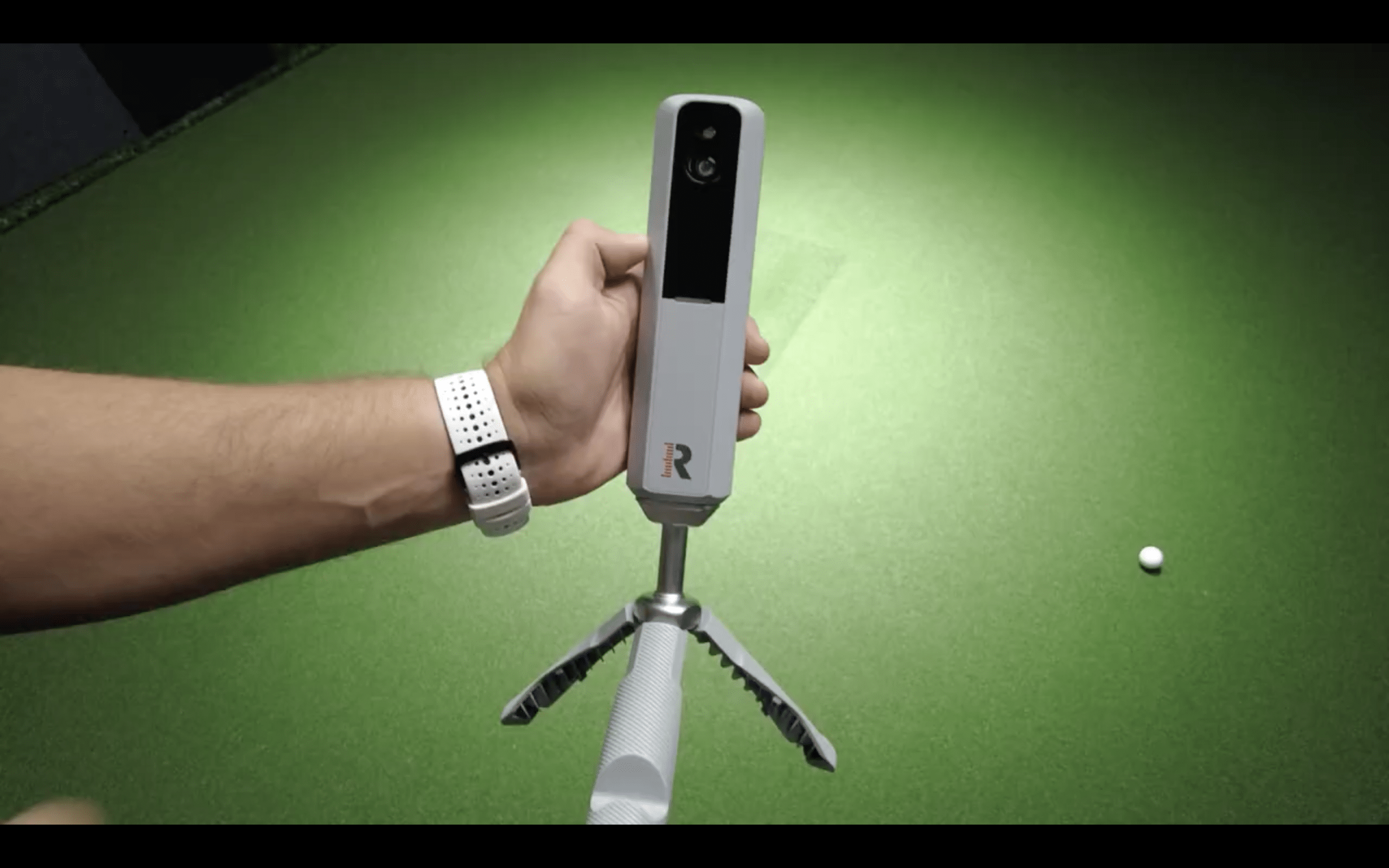 Hand holding golf launch monitor on tripod