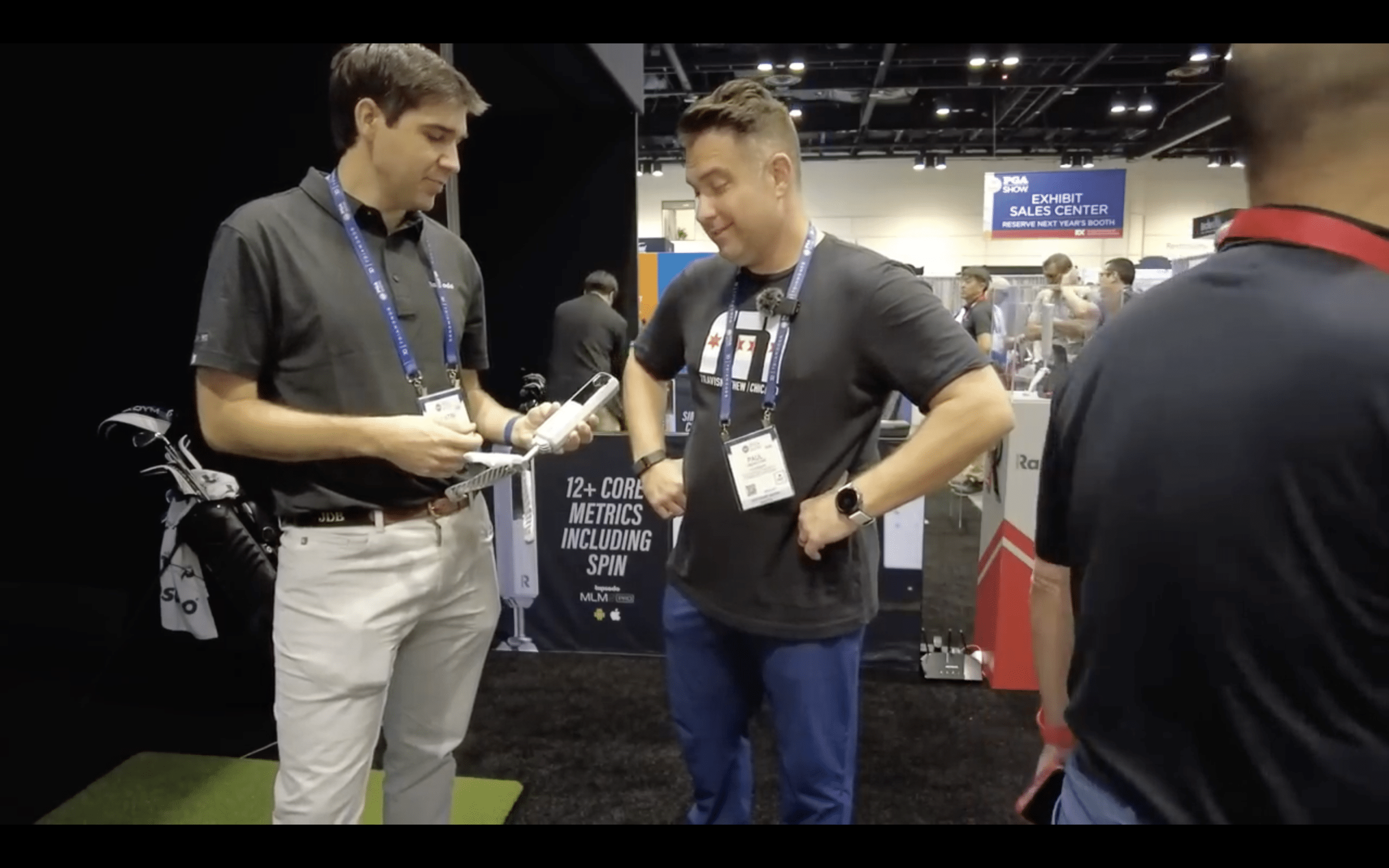 Two men discussing golf equipment at trade show booth