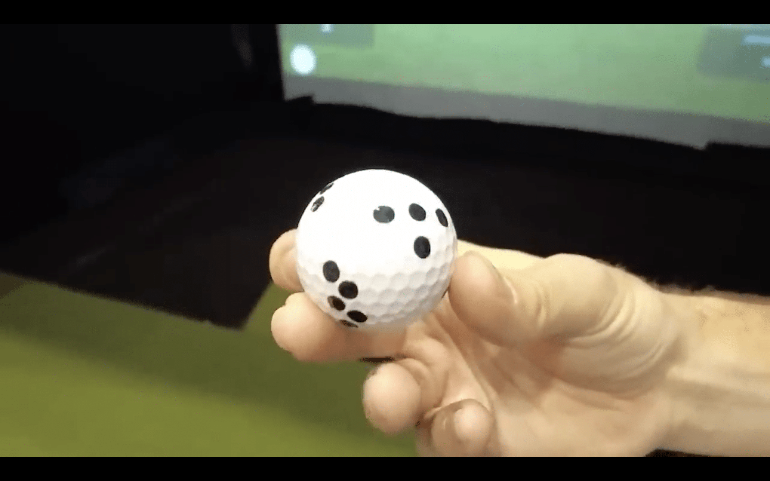 Hand holding a white golf ball with black dots