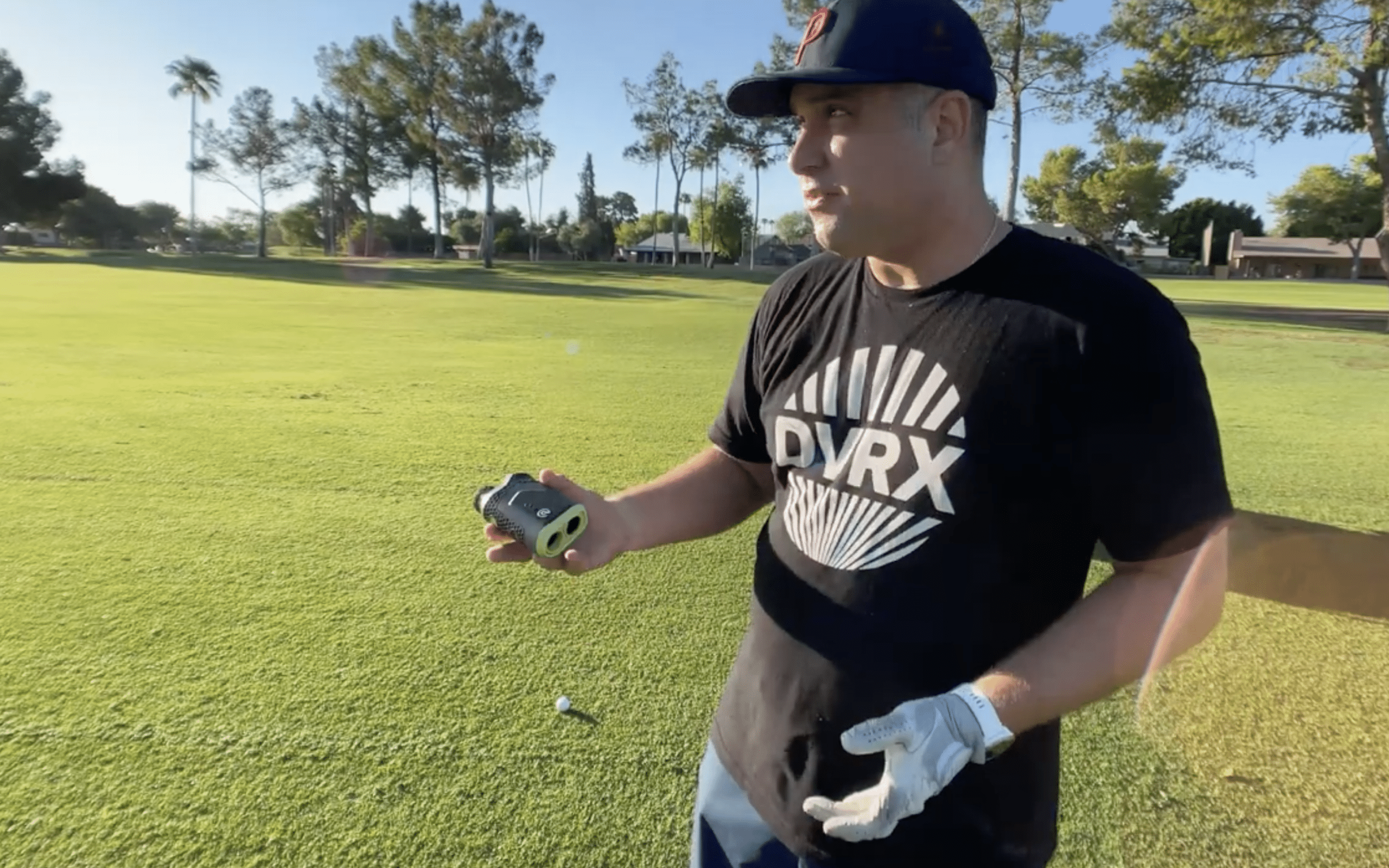 Golfer holding rangefinder on sunny golf course