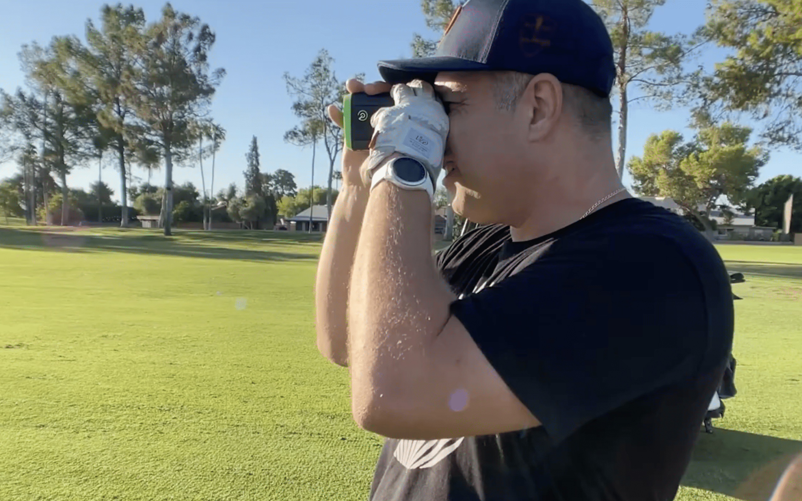 Golfer using rangefinder on sunny golf course