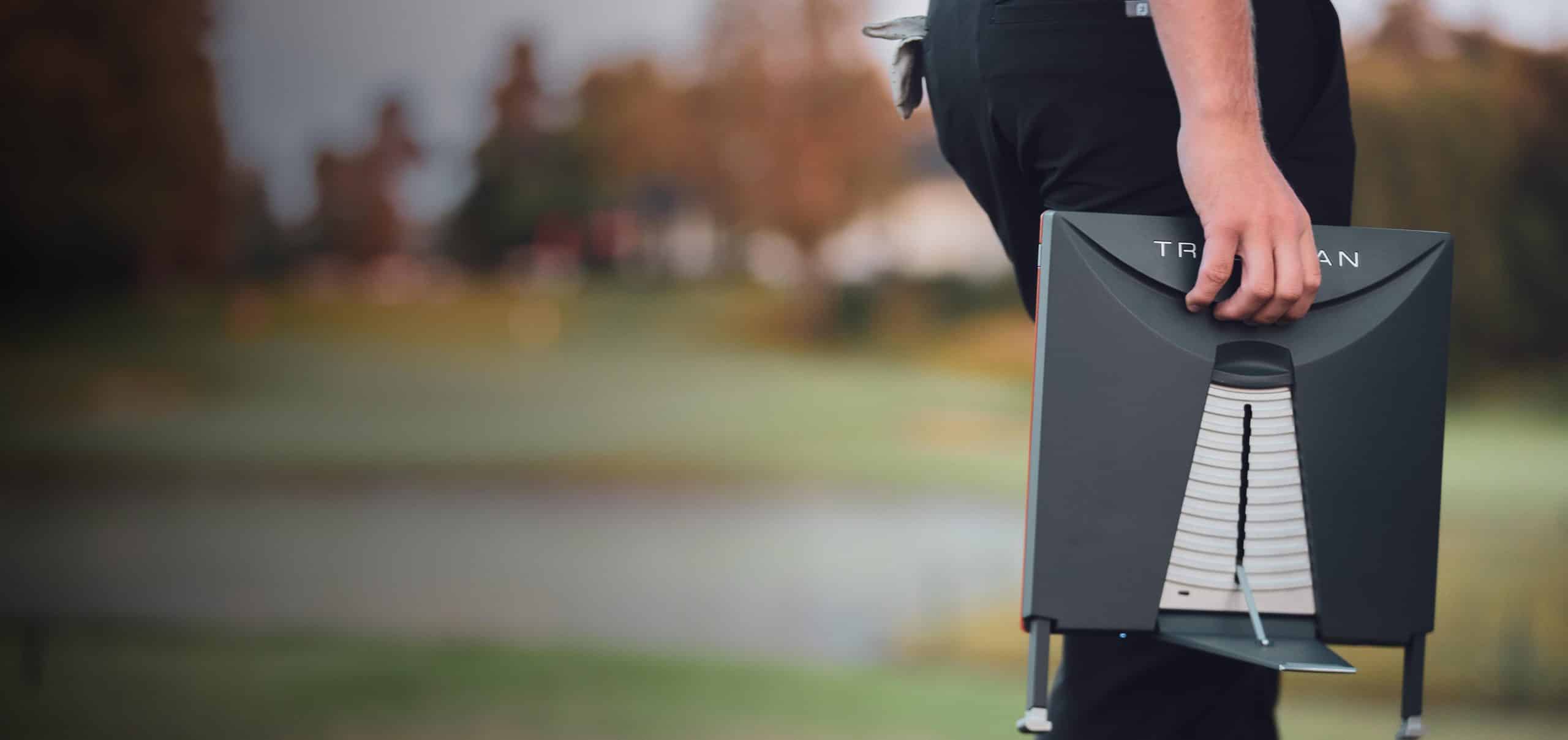 Person carrying portable golf launch monitor outdoors