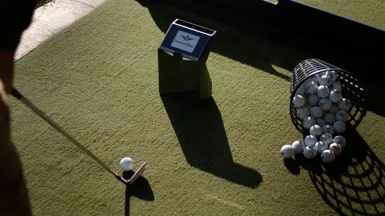 Golf club aiming at ball near basket of balls