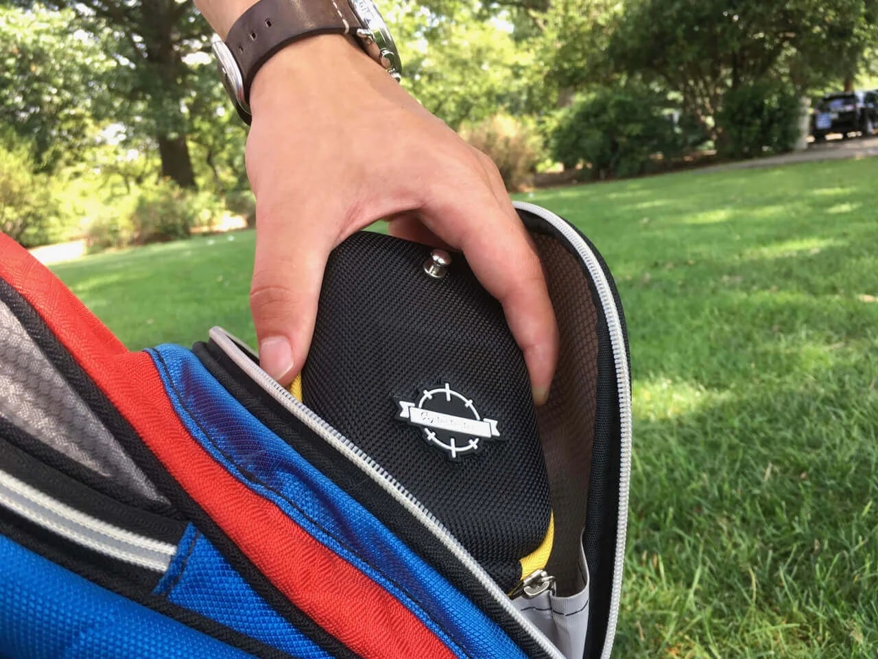 Hand placing black case into backpack outdoors
