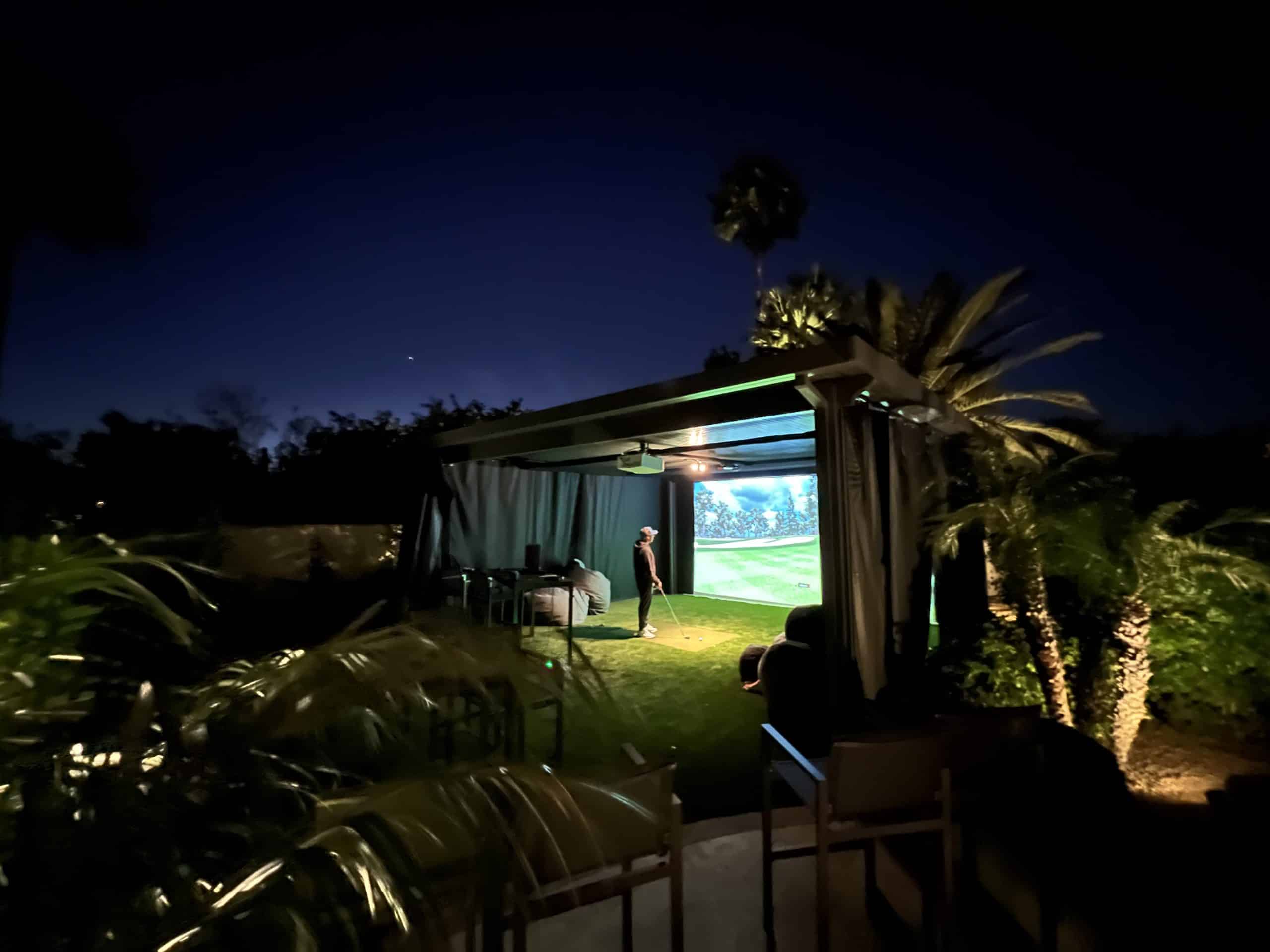 Person playing golf simulator outdoors at night