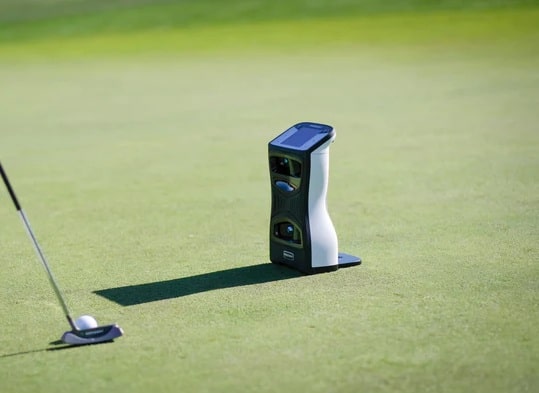 Golf launch monitor beside a putter on green