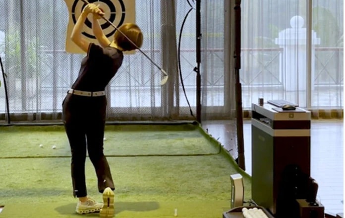Person practicing golf swing indoors with simulator