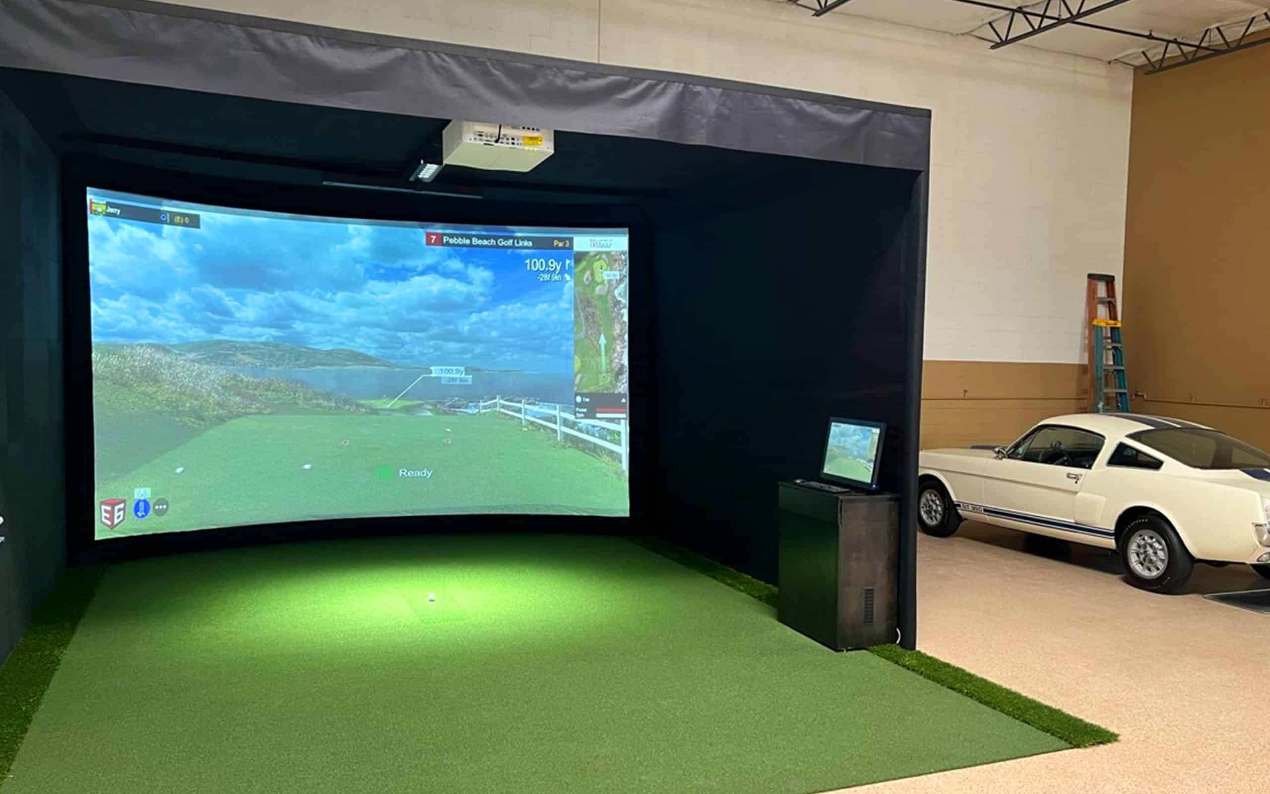 Indoor golf simulator setup beside classic white car