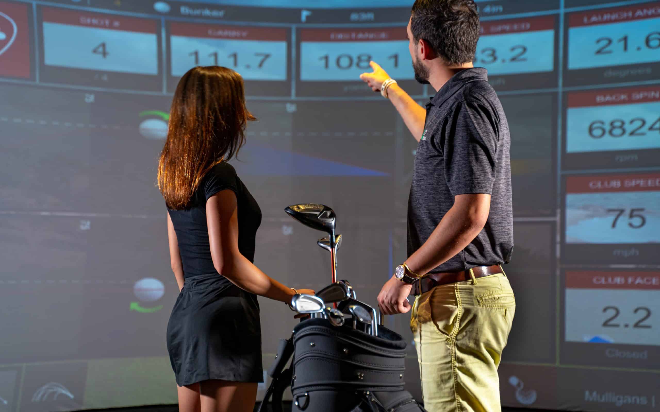 Golfers analyzing swing data on simulator screen