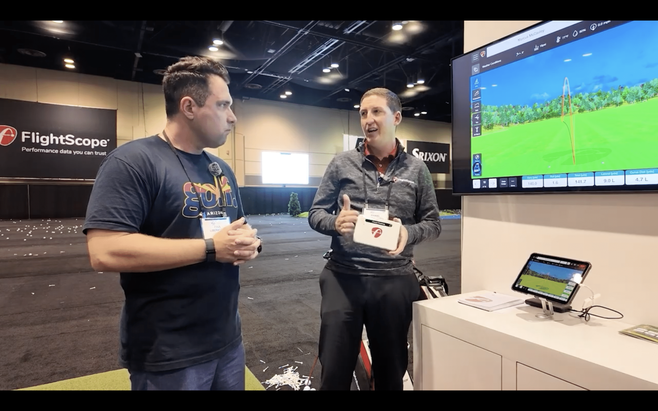 Two men discussing golf simulator technology at convention.