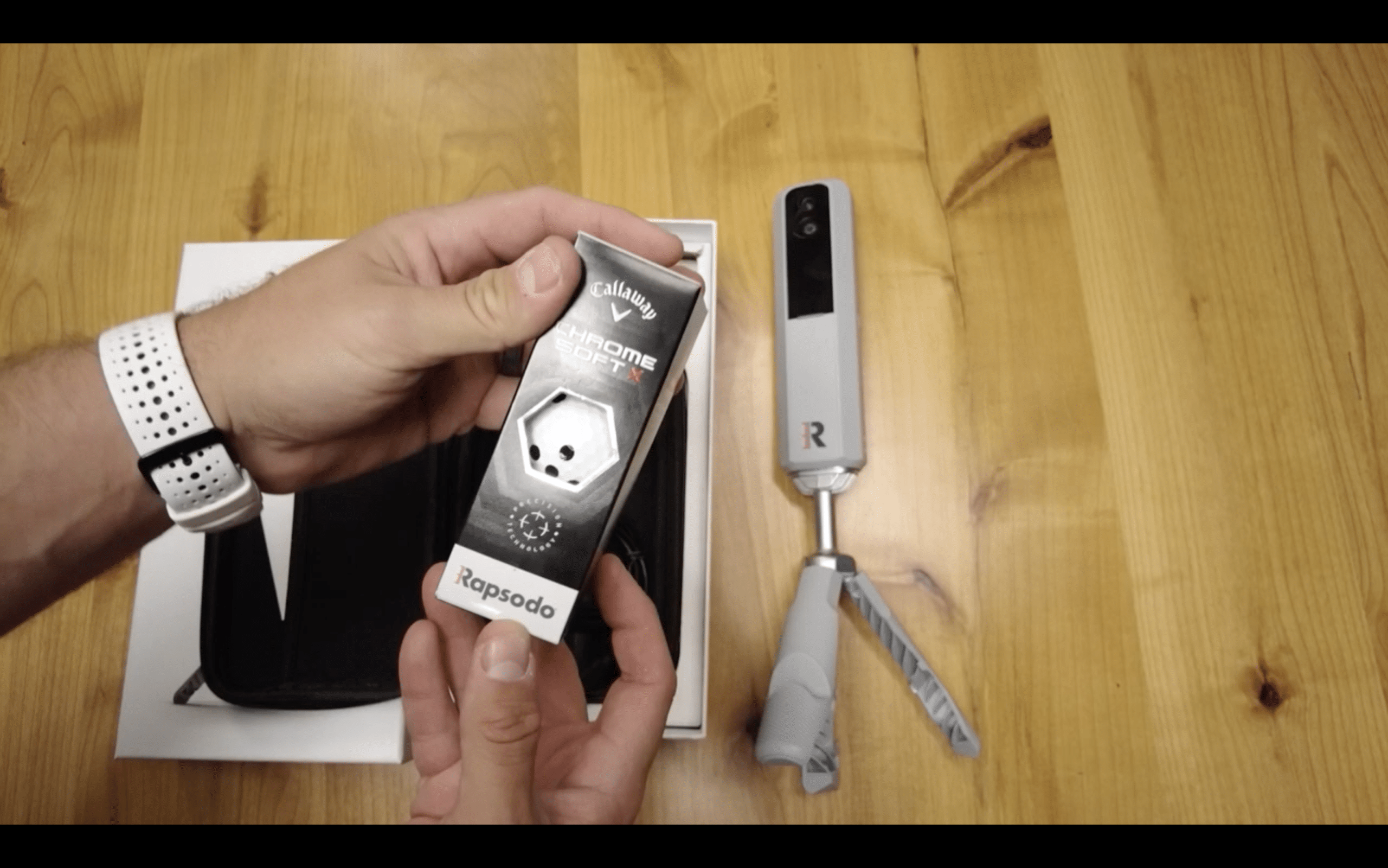 Person holding golf ball box beside launch monitor