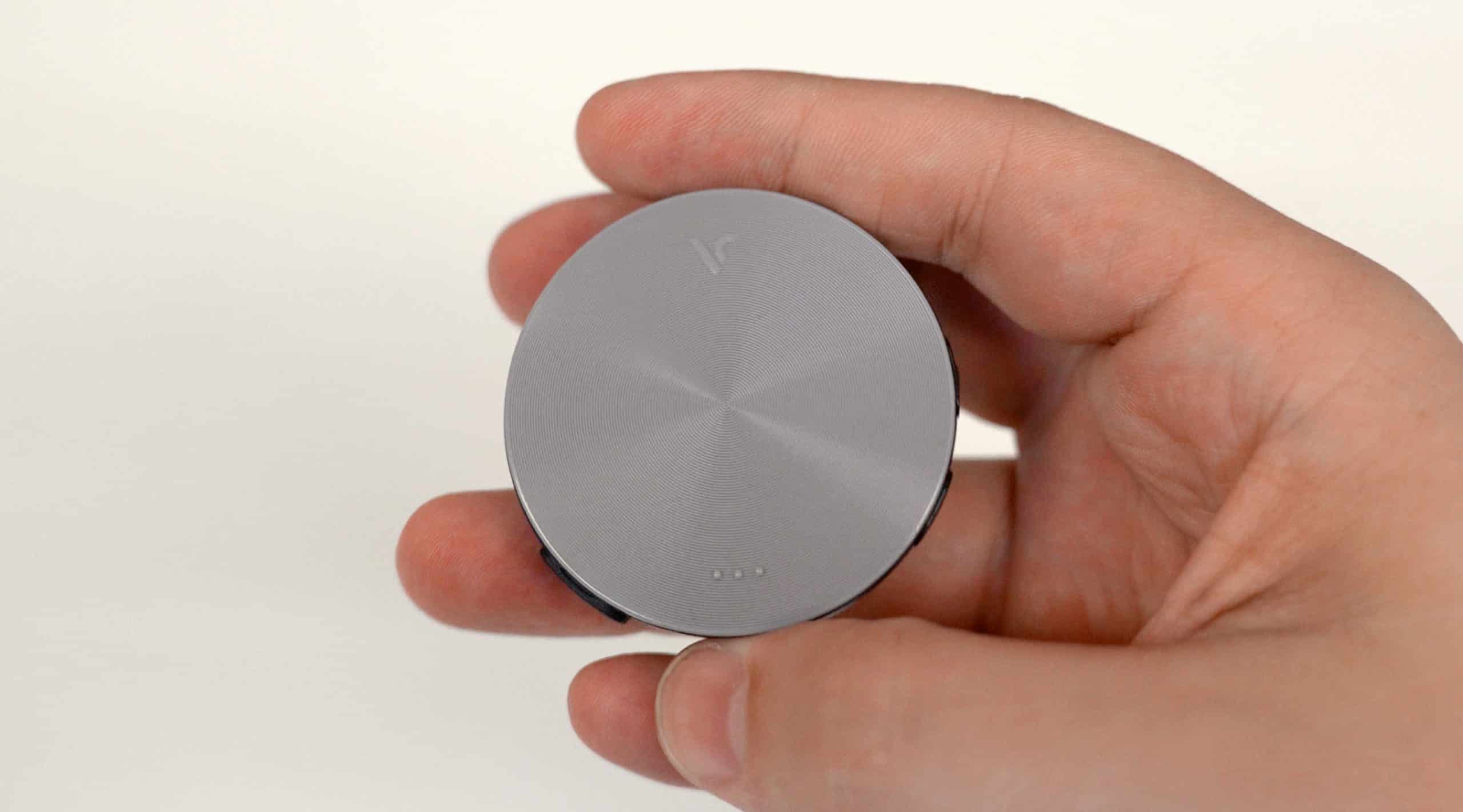 Hand holding a small round silver gadget