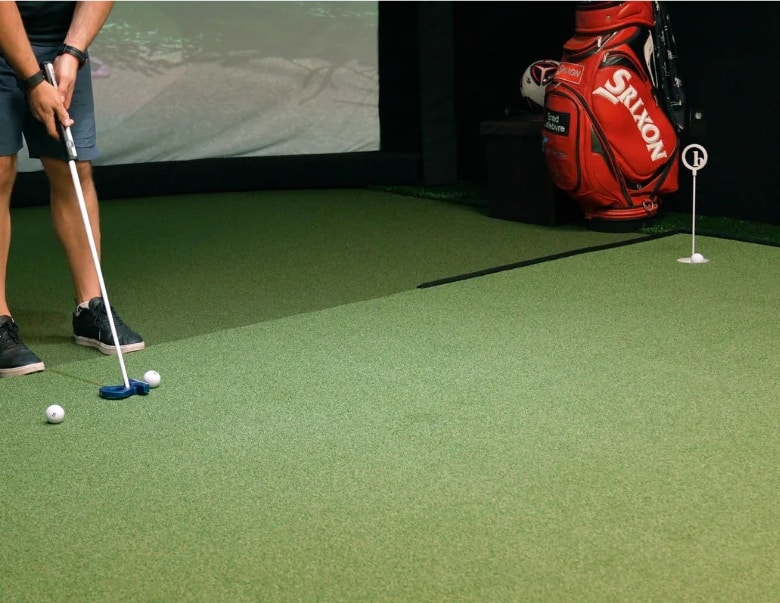 Golfer putting on indoor green with equipment bag
