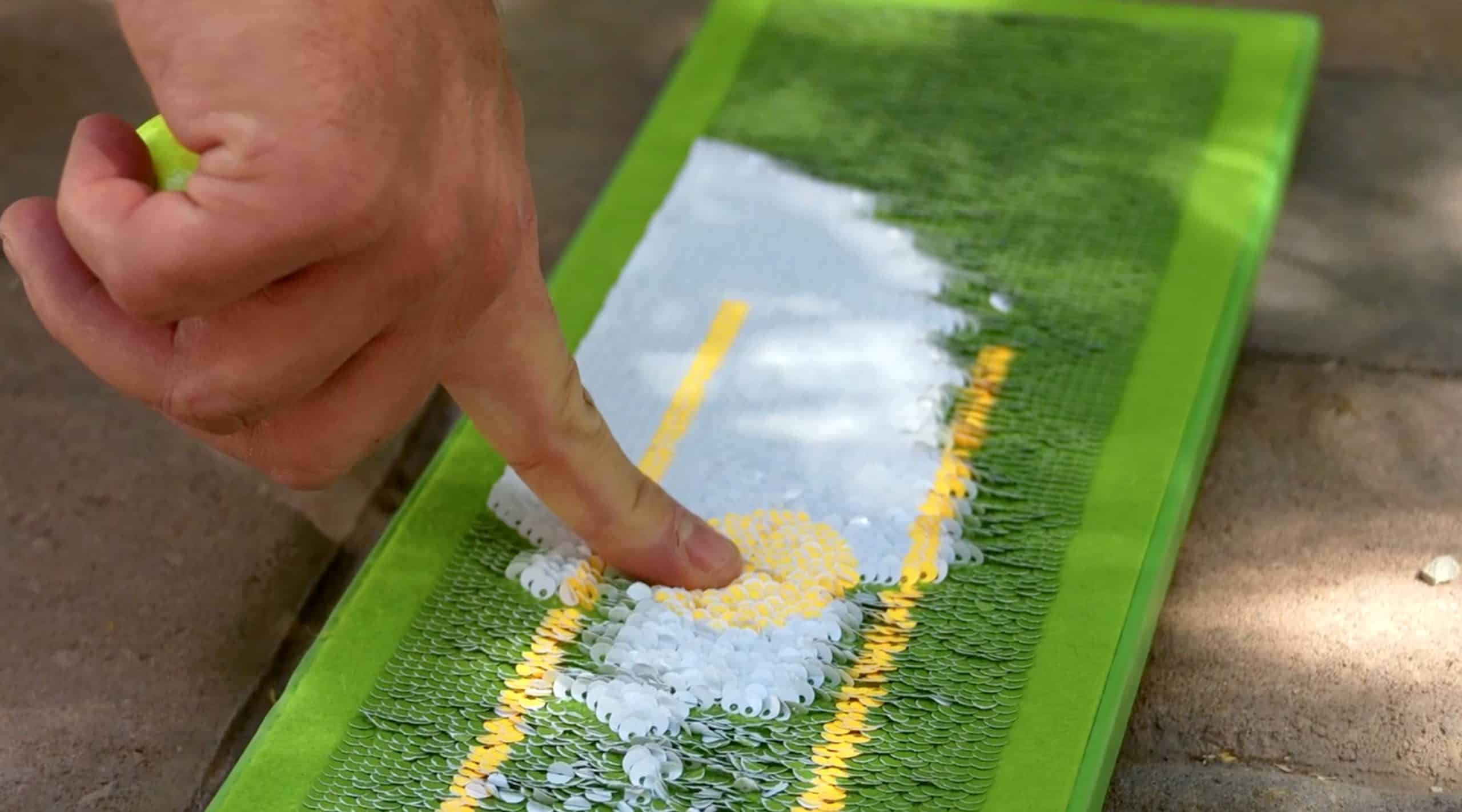 Hand touching sequined art on green surface