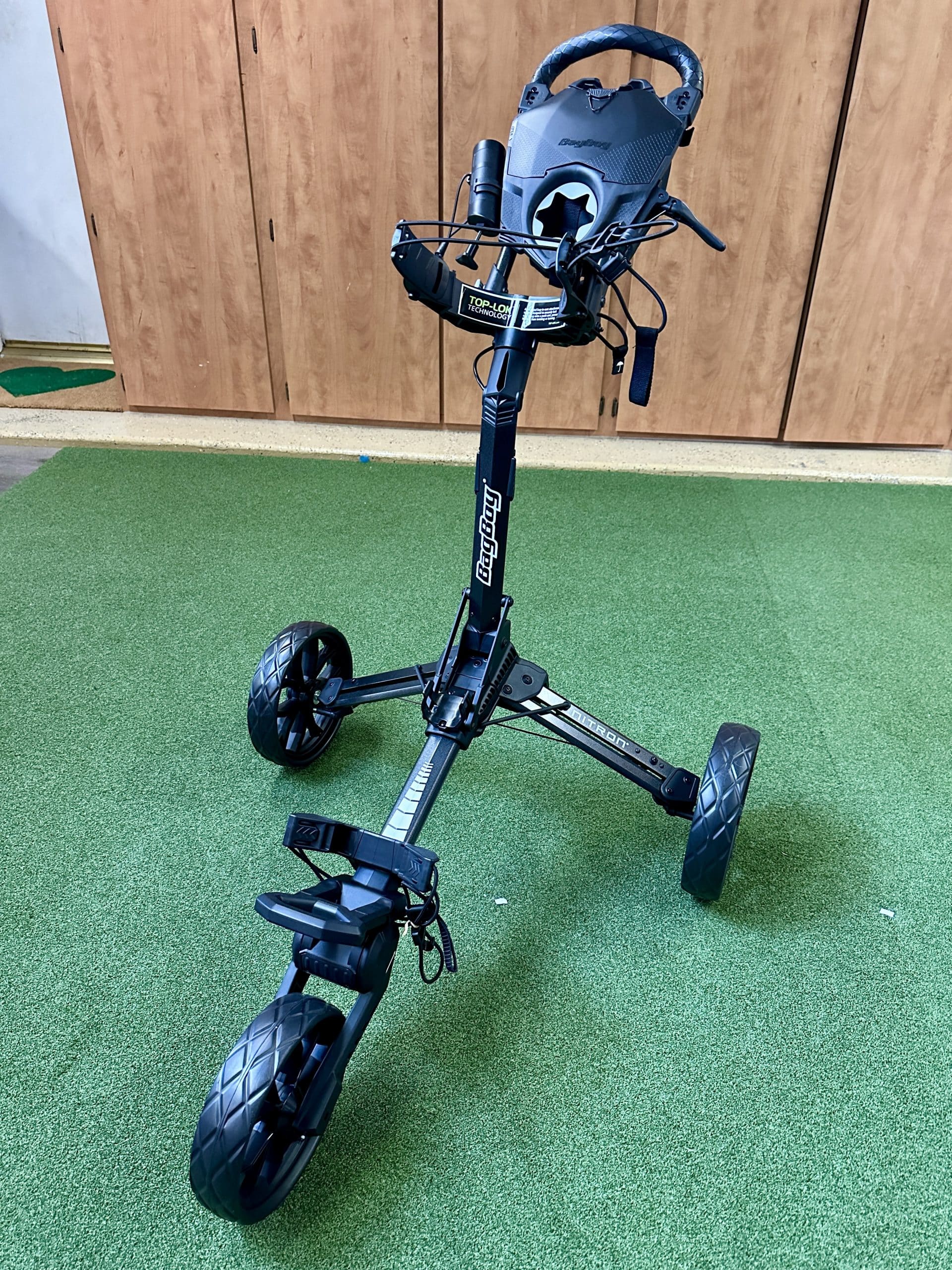 Black three-wheel golf push cart on green turf