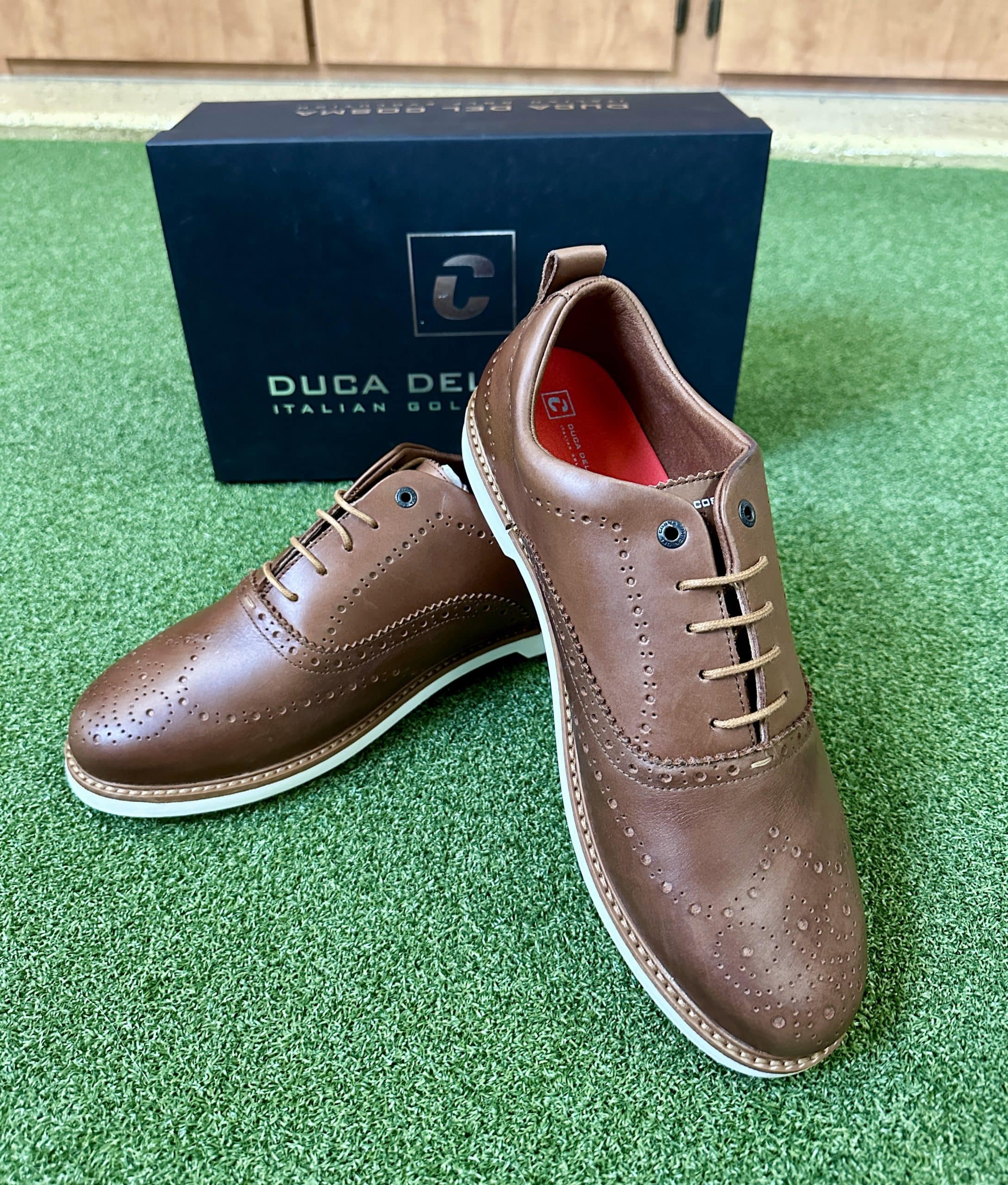 Brown leather brogue shoes on green turf.
