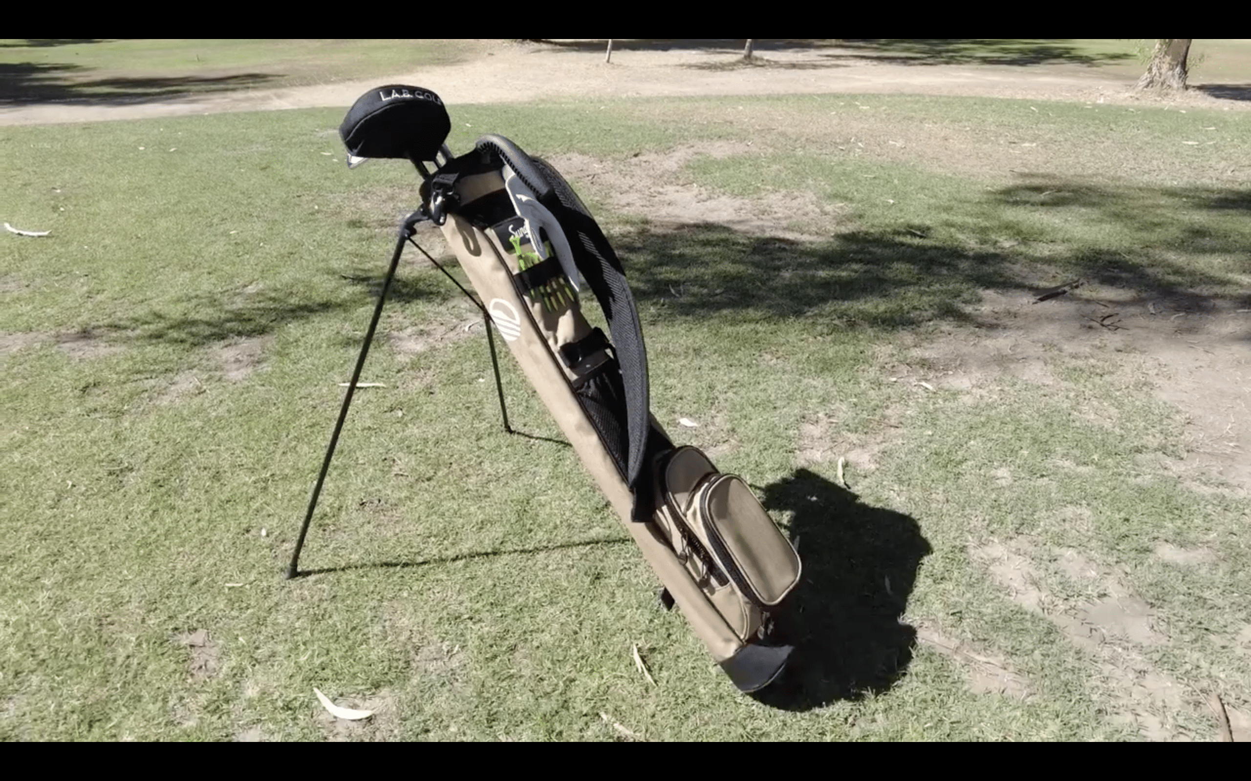 Golf bag standing on grassy course.